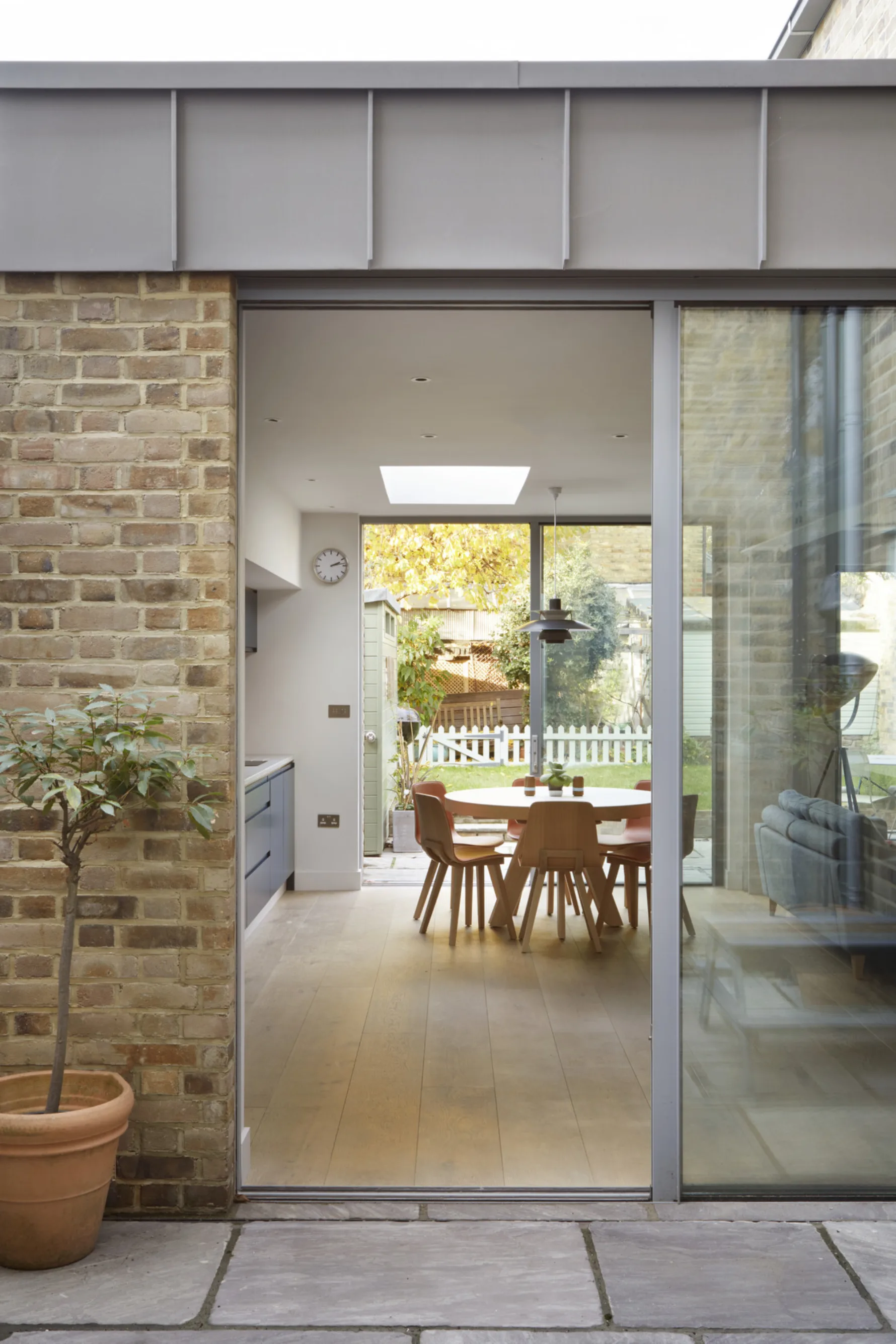 Dining area framed by exposed steel structure with large sliding doors opening to the garden and courtyard