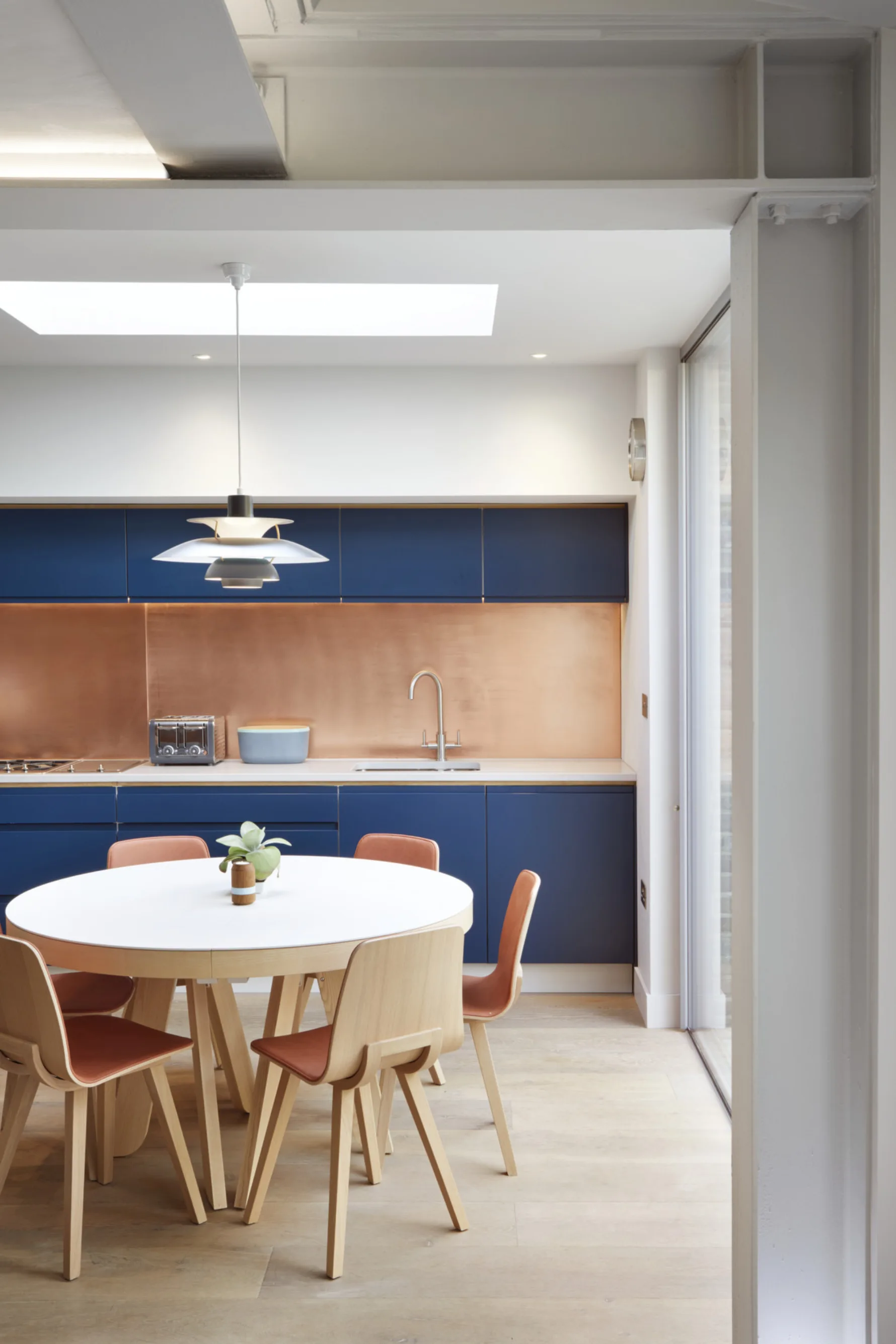Open-plan kitchen viewed through exposed structural steelwork, highlighting the relationship between the original house and the new extension