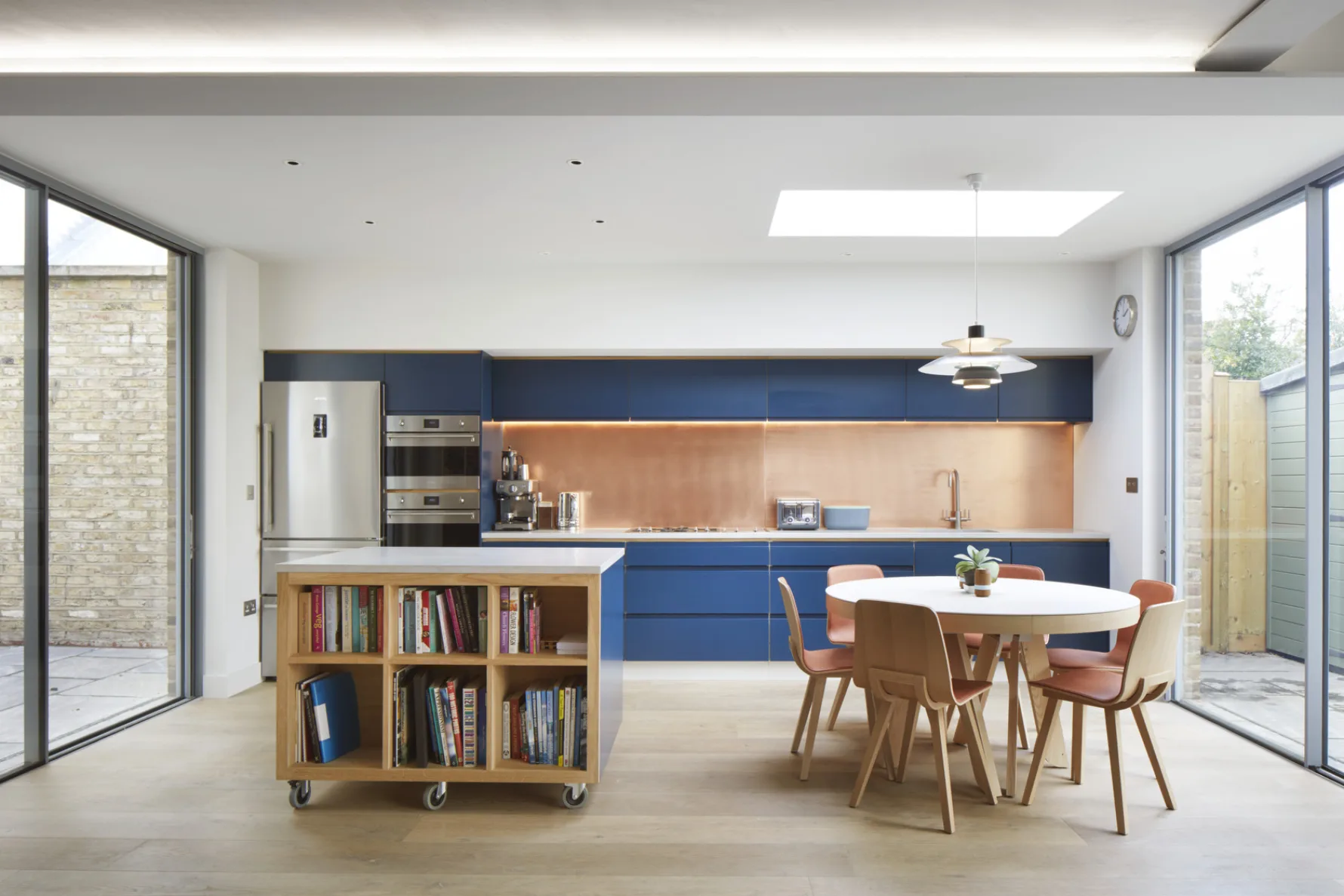 Light-filled kitchen extension with blue cabinetry, copper splashback, rooflight and sliding doors to the courtyard and garden