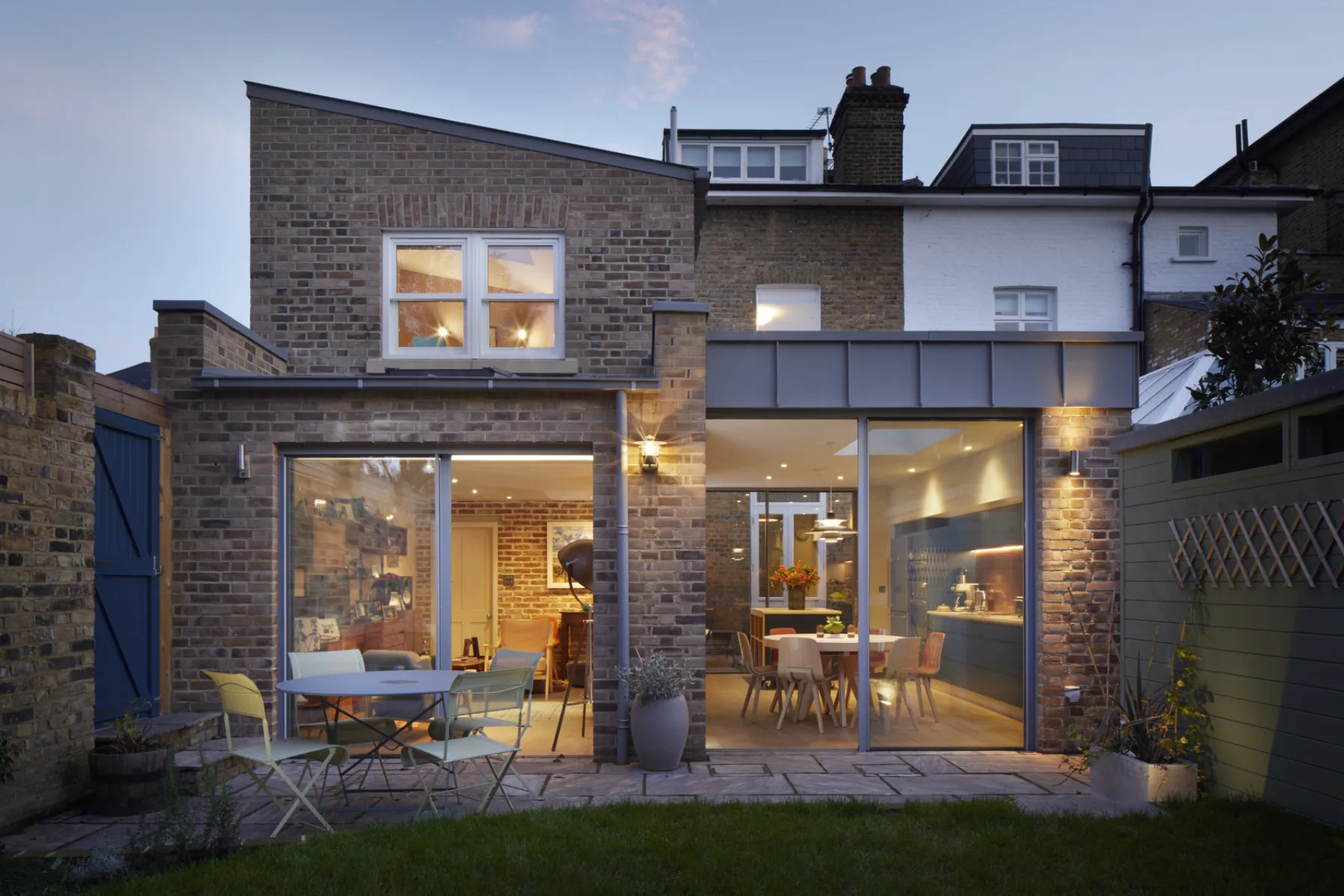 Twilight view of the completed rear extension showing brickwork, zinc detailing and garden-facing elevations.