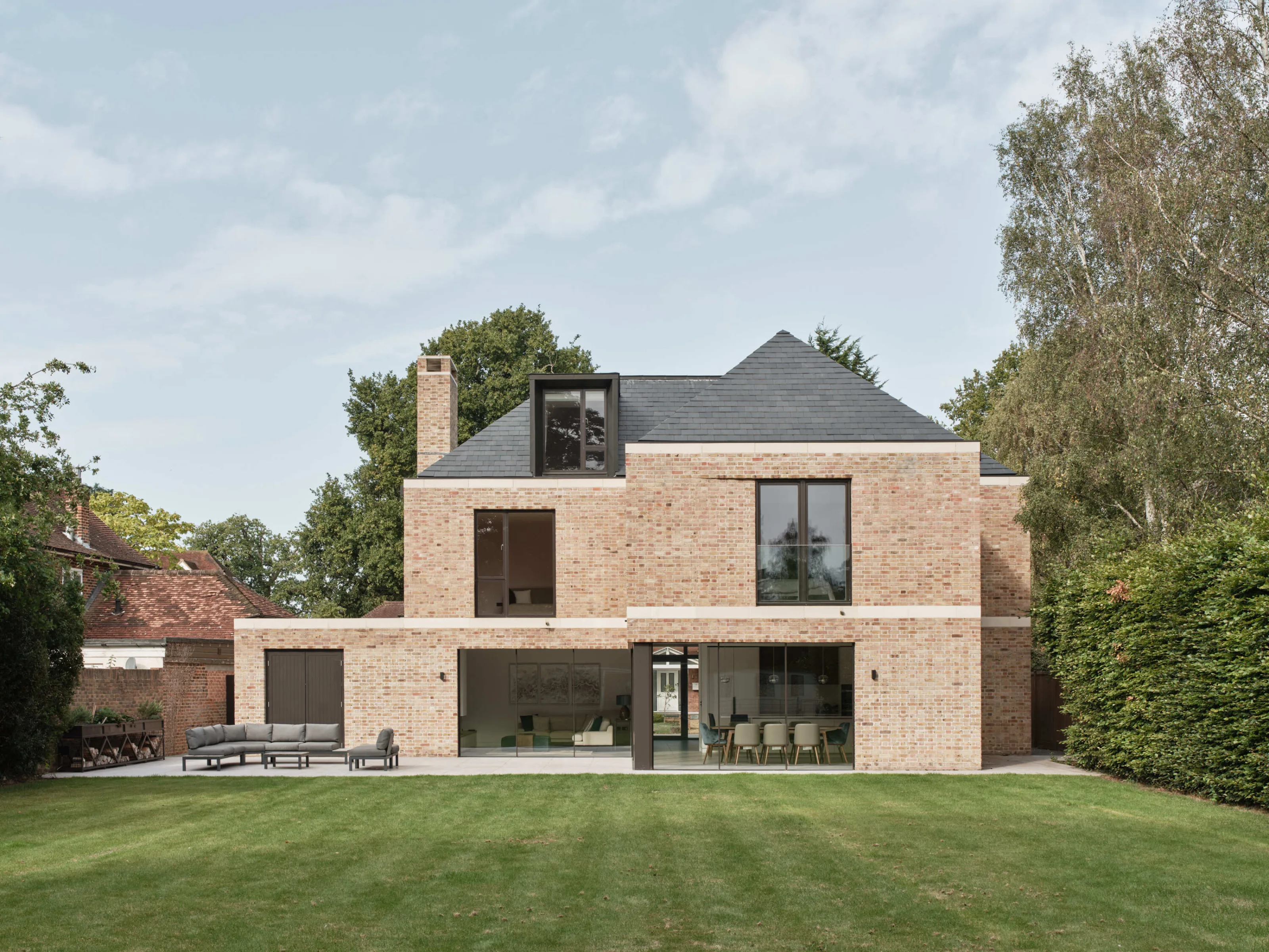 Modern brick house with terrace, outdoor seating area, and open-plan interior visible through glazing