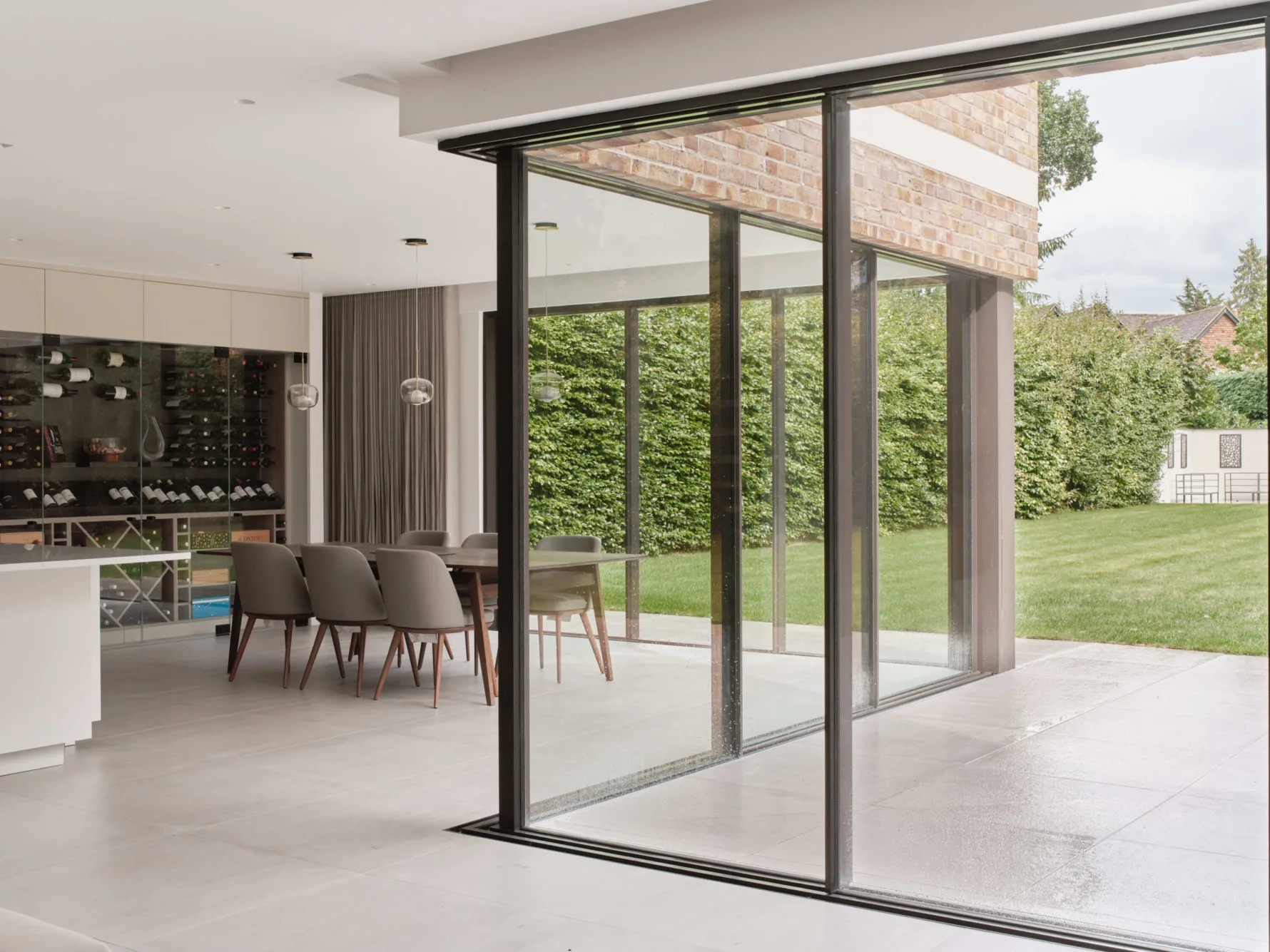 Open-plan kitchen diner with glazing opening onto stone paved terrace and garden beyond
