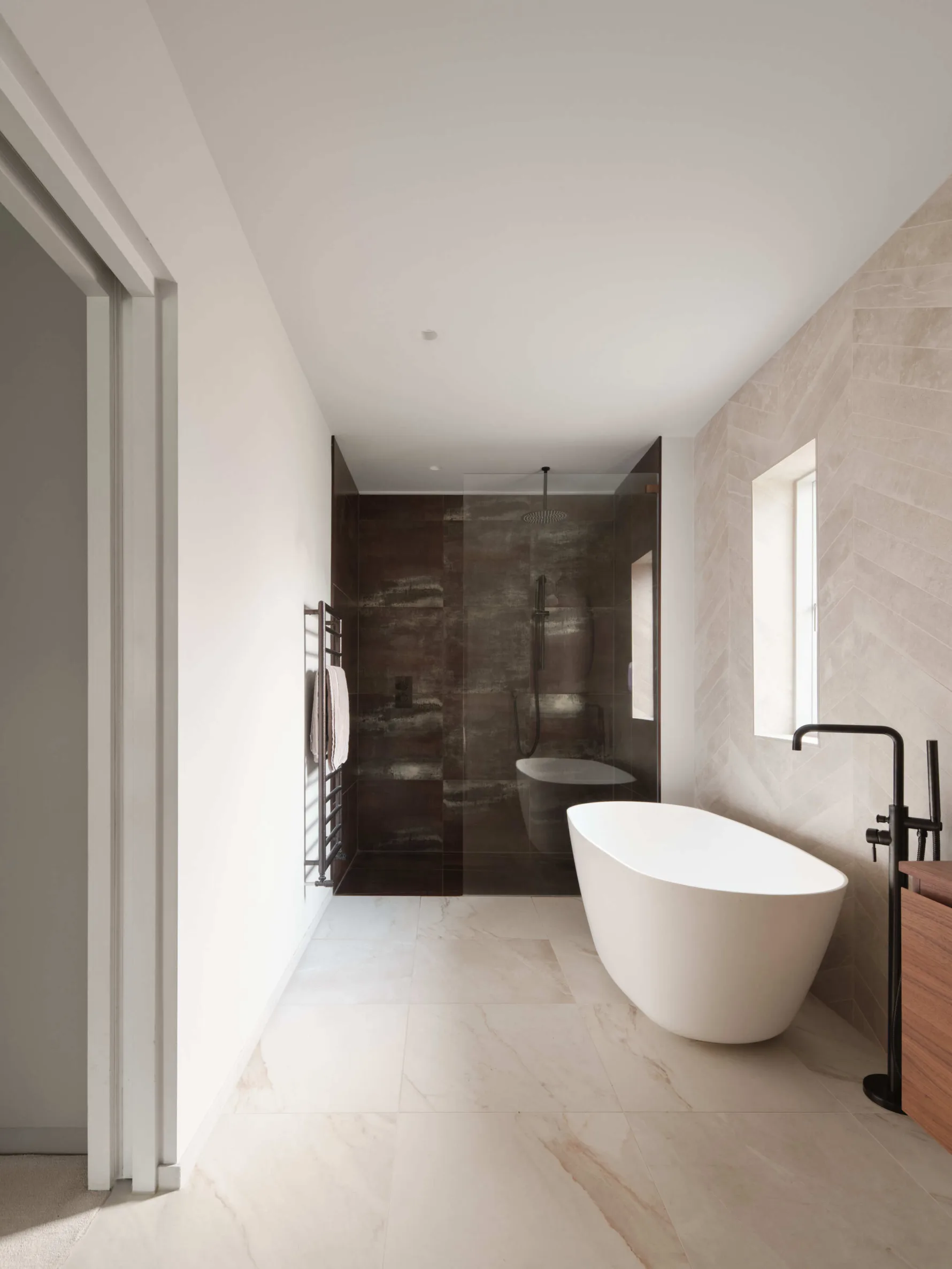 Modern minimalist bathroom with freestanding bathtub and glass walk-in shower with dark tiles.