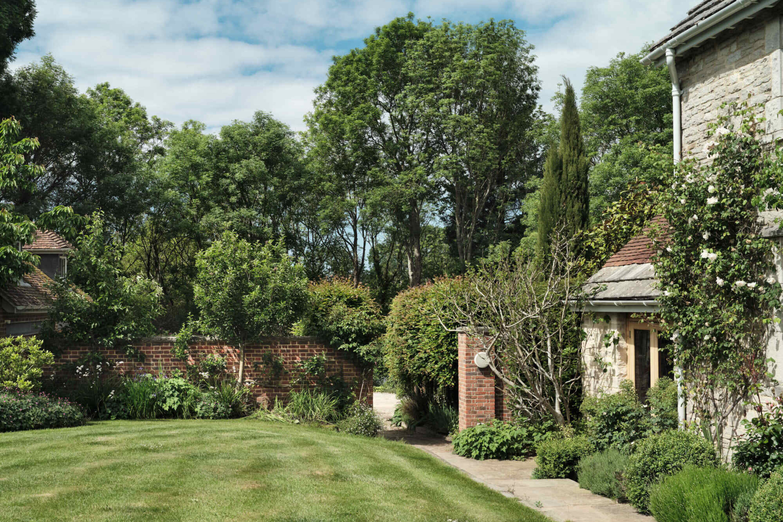 Courtyard garden at Corfe Castle House with lawn, stone paving, climbing plants and mature trees surrounding the house.