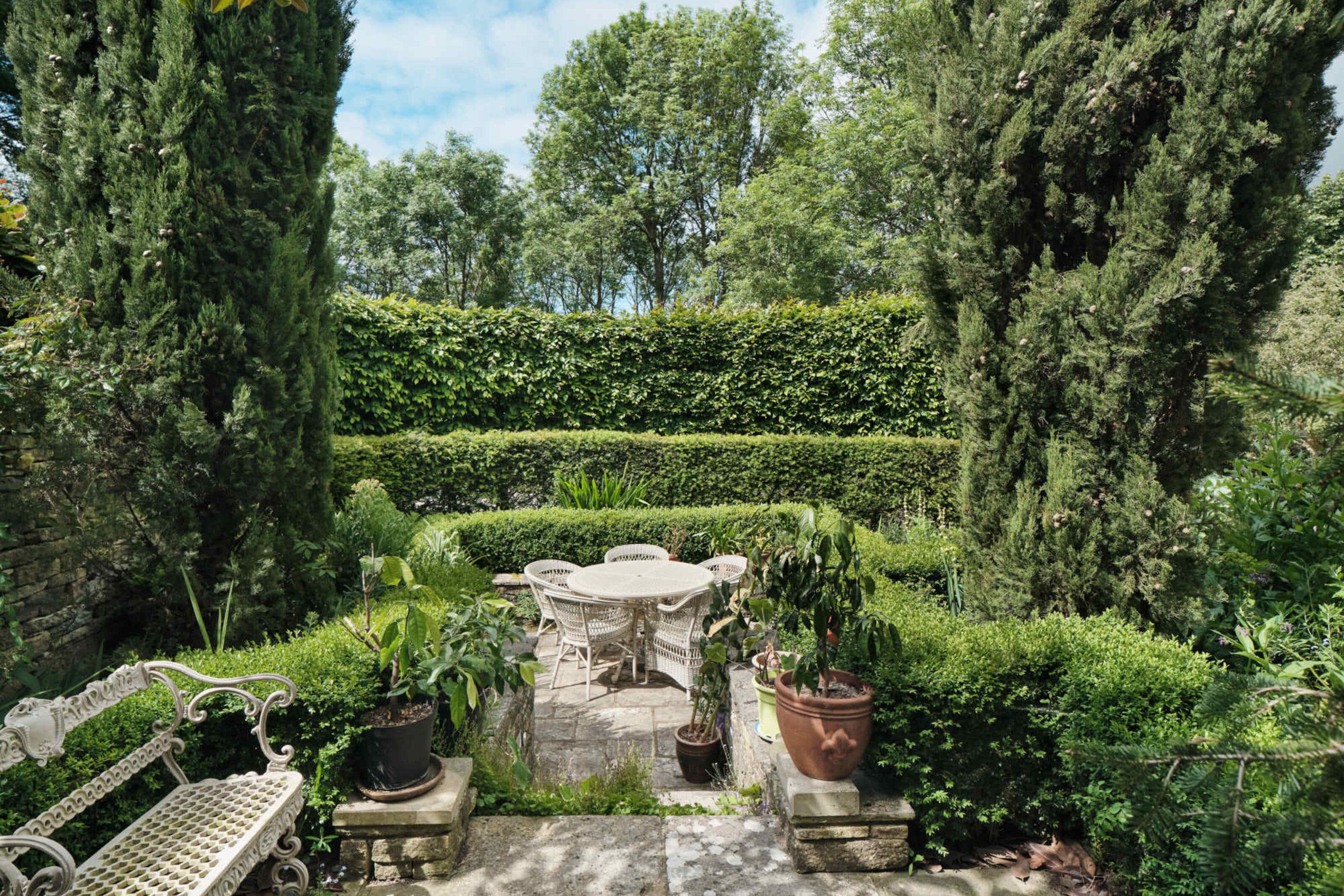 Formal garden terrace at Corfe Castle House with clipped box hedging, stone paving, outdoor seating and mature cypress trees.