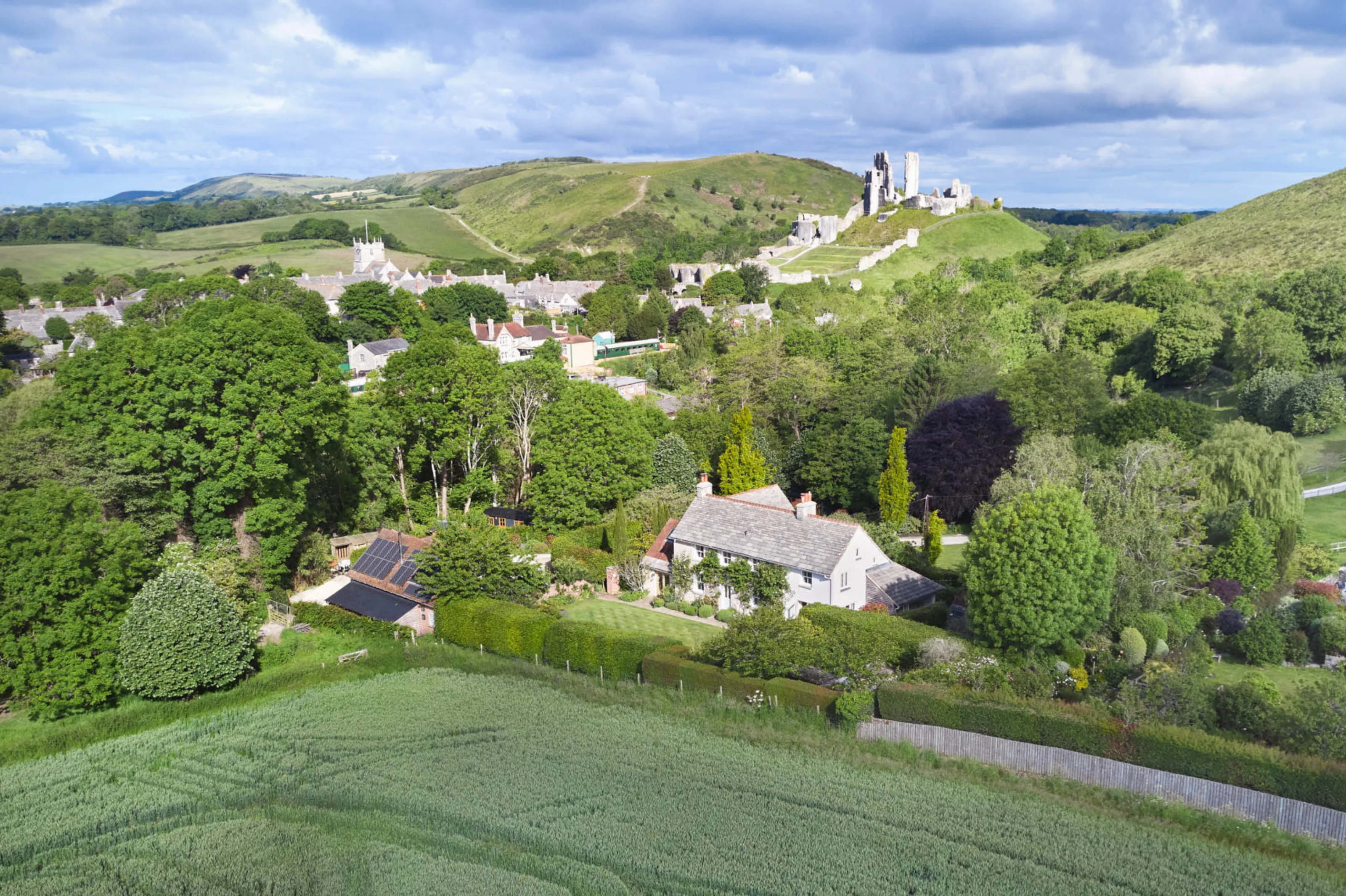 Aerial view showing Corfe Castle House, surrounding gardens and farmland, with Corfe Castle and the Dorset countryside beyond.
