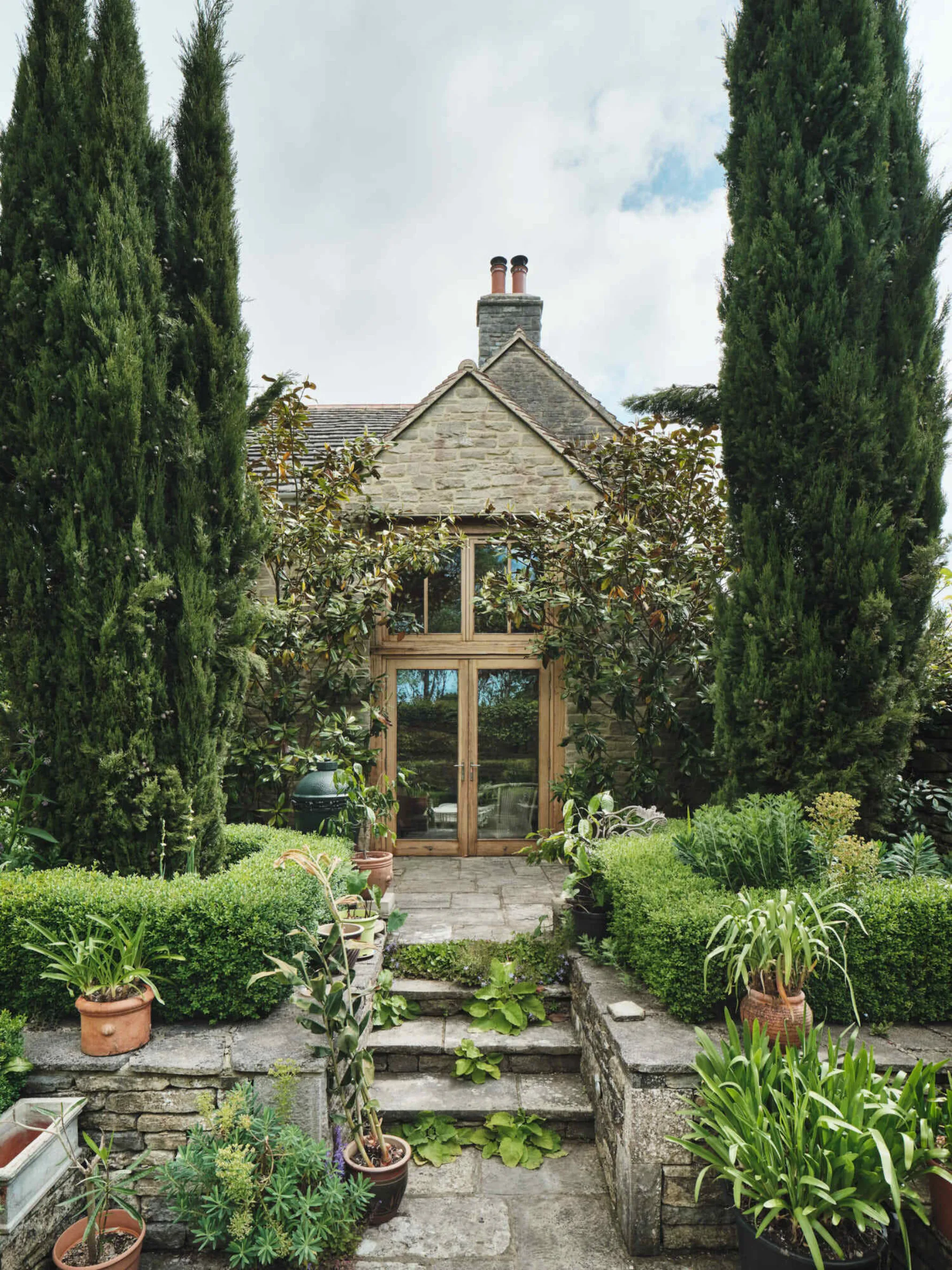 Garden room elevation at Corfe Castle House, framed by mature planting, stone terraces and clipped hedging.