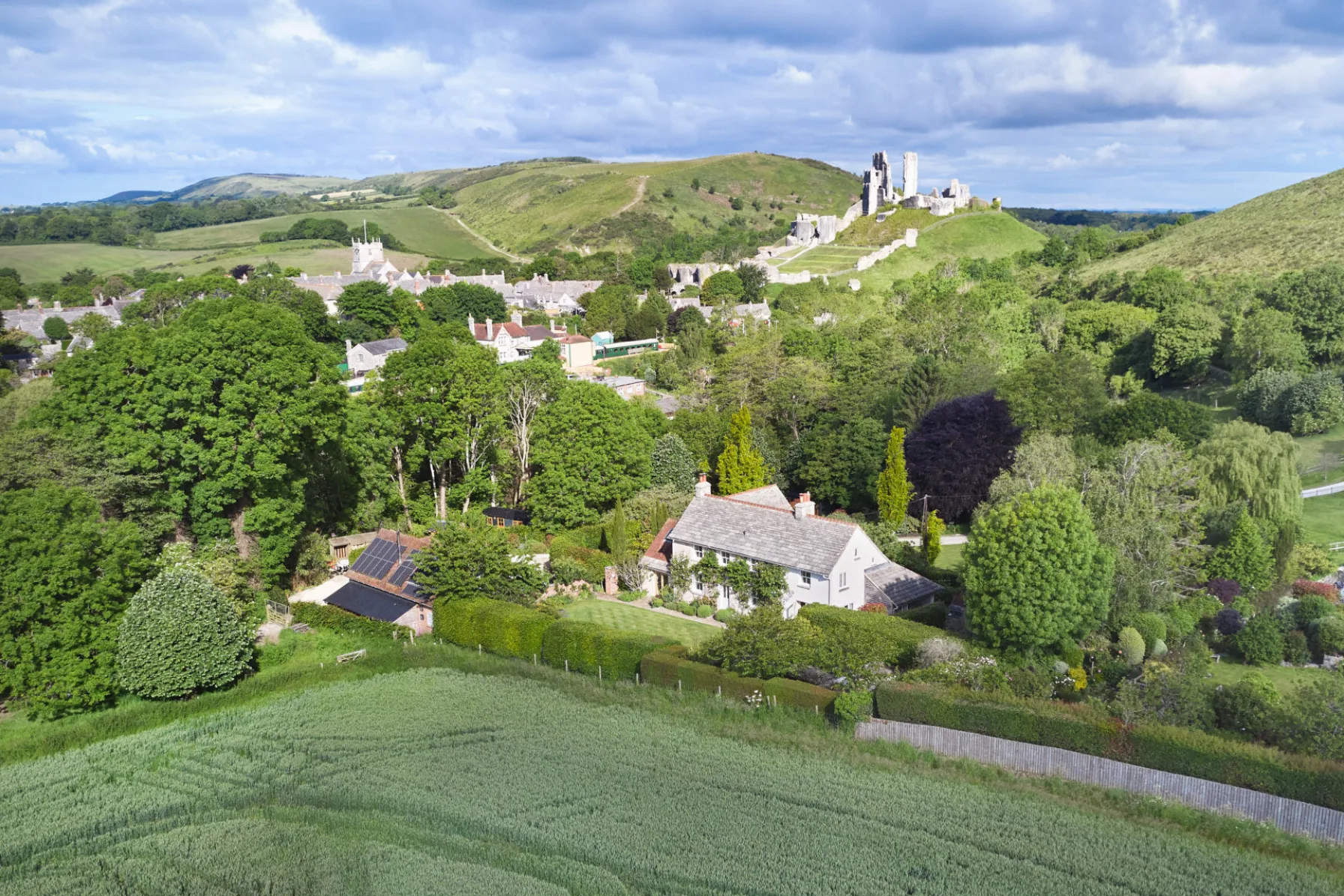 Aerial view showing Corfe Castle House, surrounding gardens and farmland, with Corfe Castle and the Dorset countryside beyond.