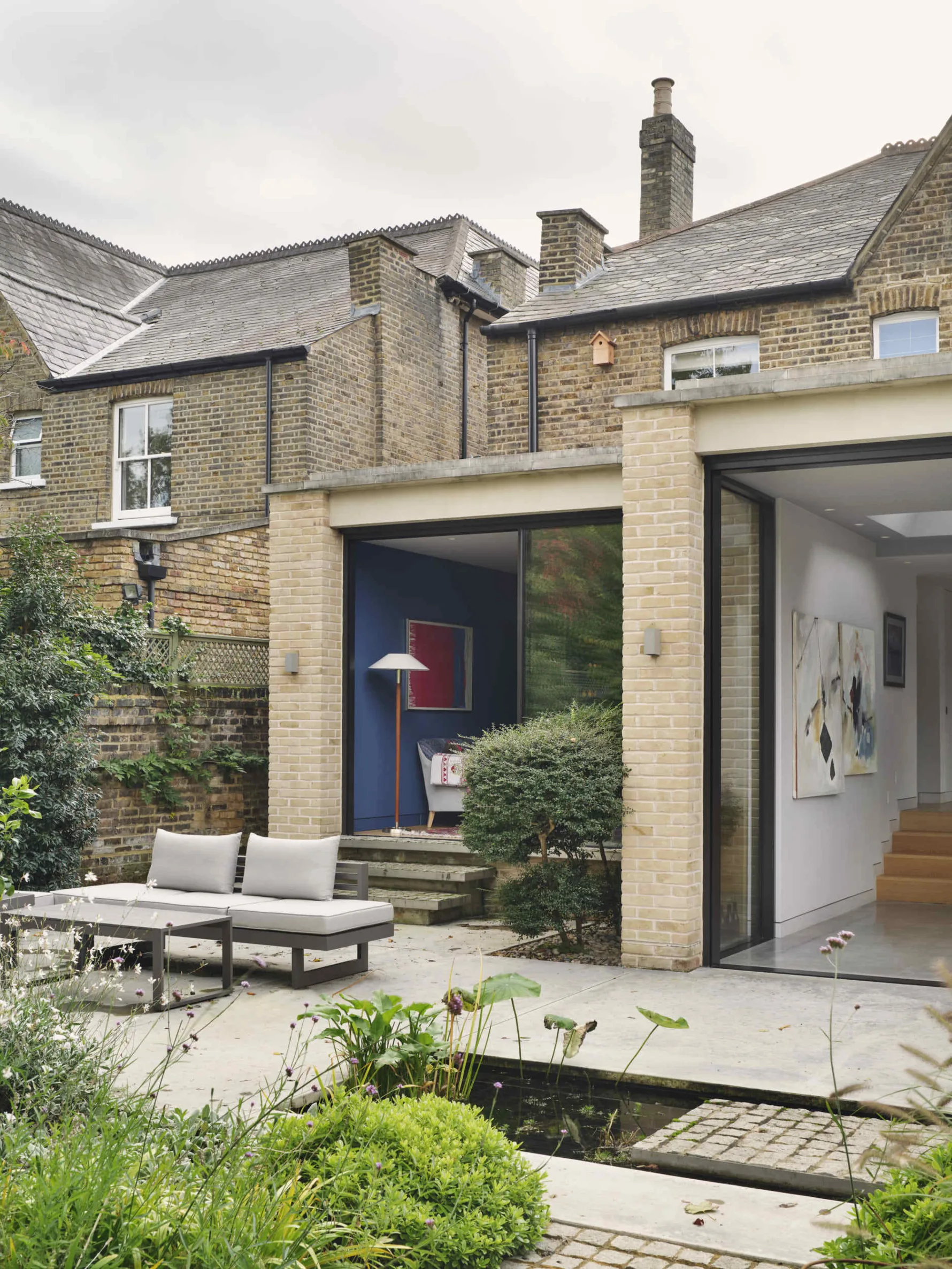 Rear view of Kew House showing a contemporary brick garden pavilion extension with large sliding glass doors opening onto a landscaped garden.