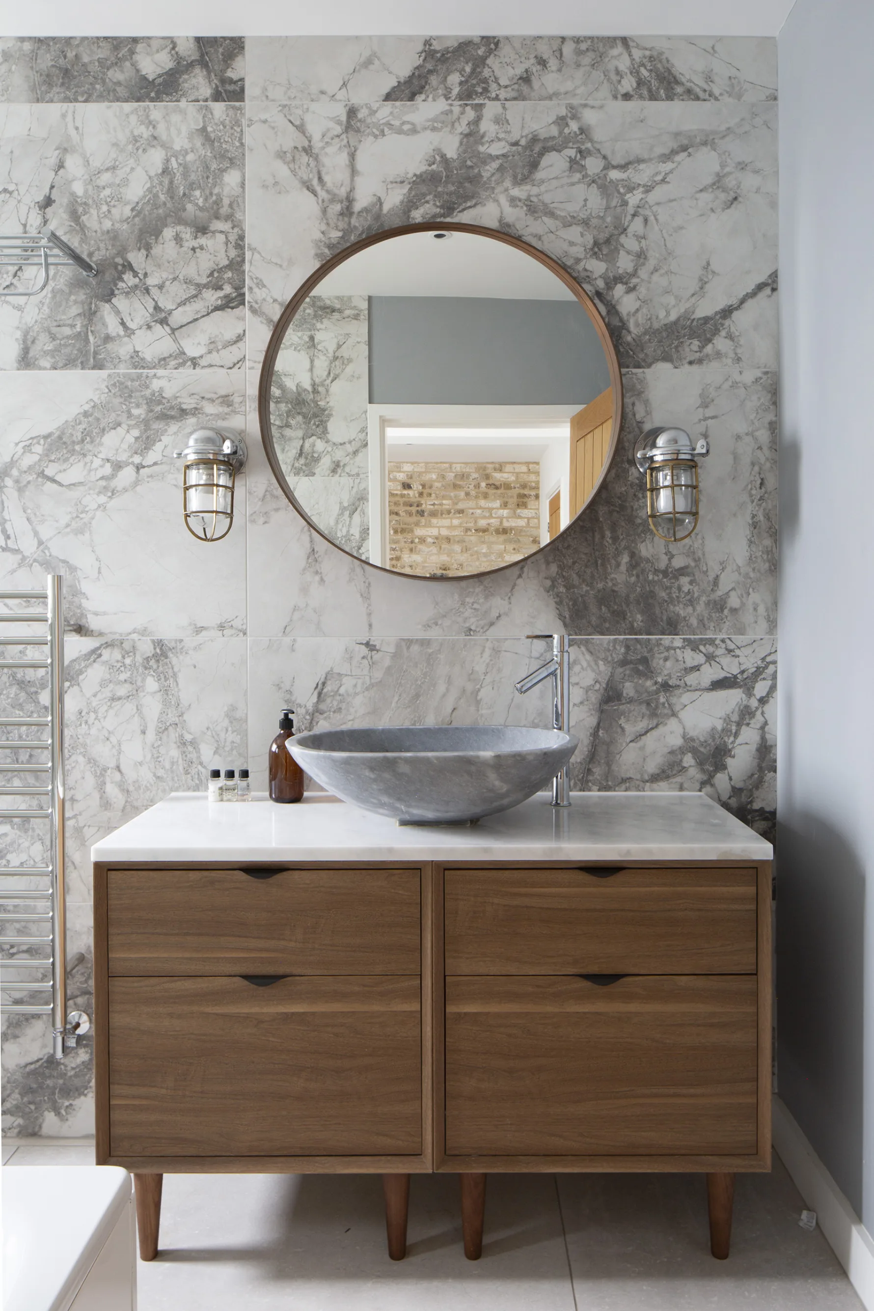 Contemporary bathroom with marble wall tiles, timber vanity unit and circular mirror in renovated home