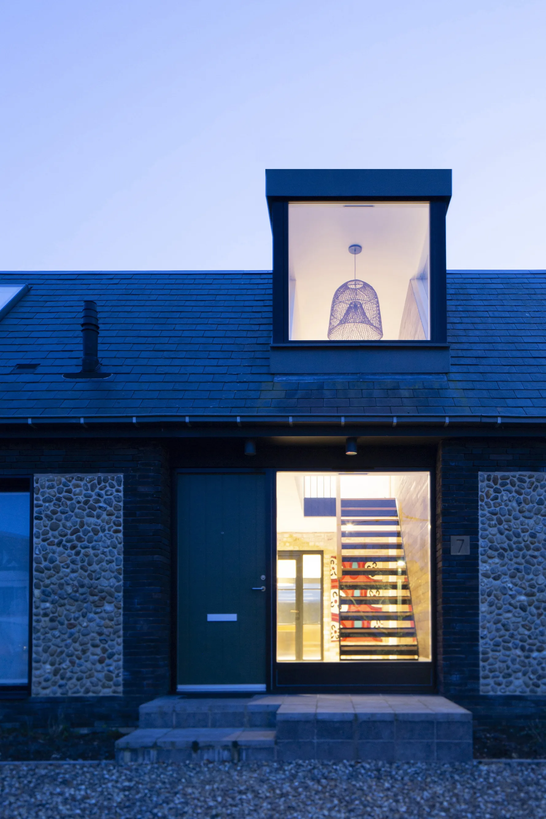 Front entrance with illuminated dormer window and exposed staircase at dusk in Old Hunstanton house