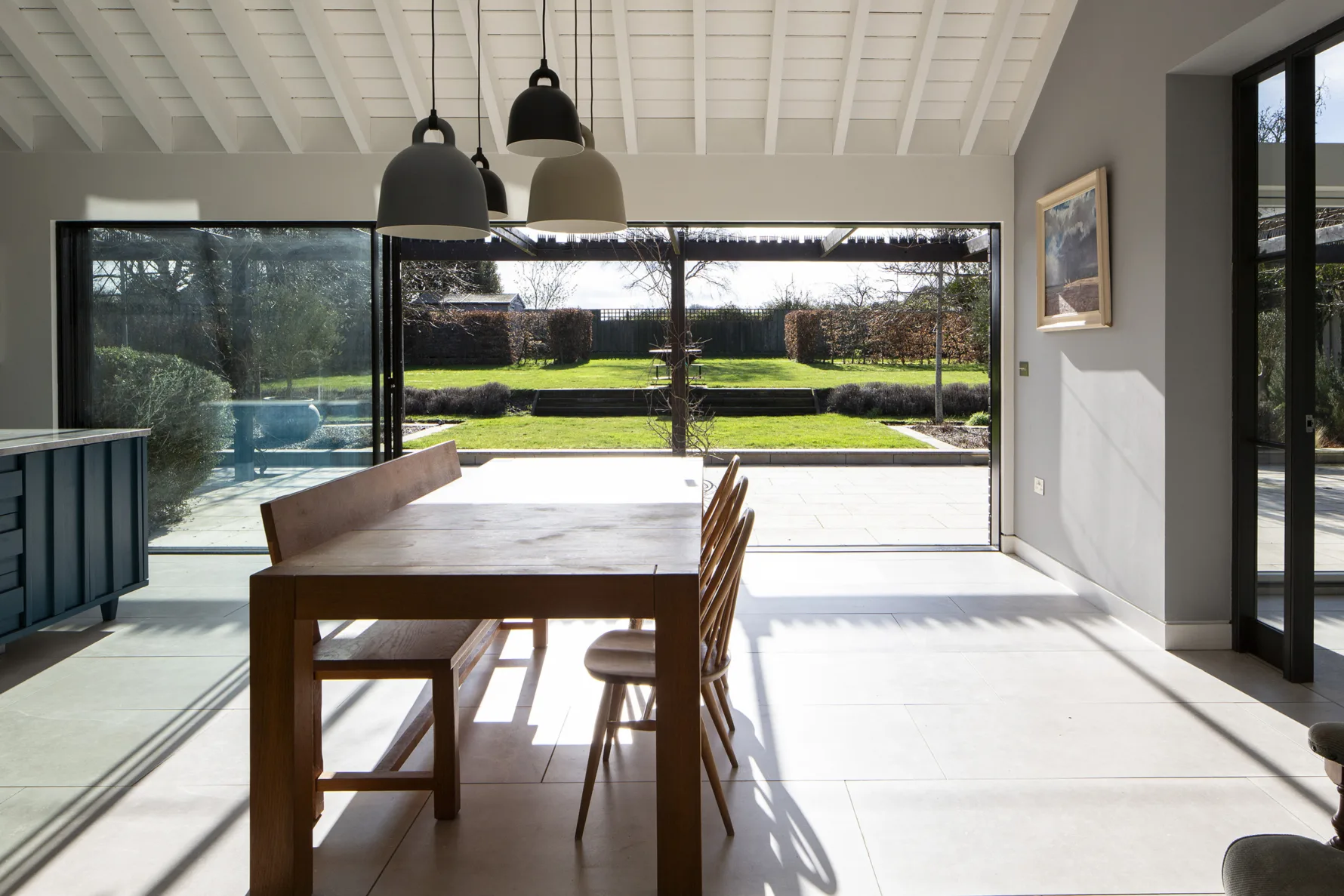 Open-plan dining area with vaulted ceiling and large sliding glazing opening onto garden and pergola