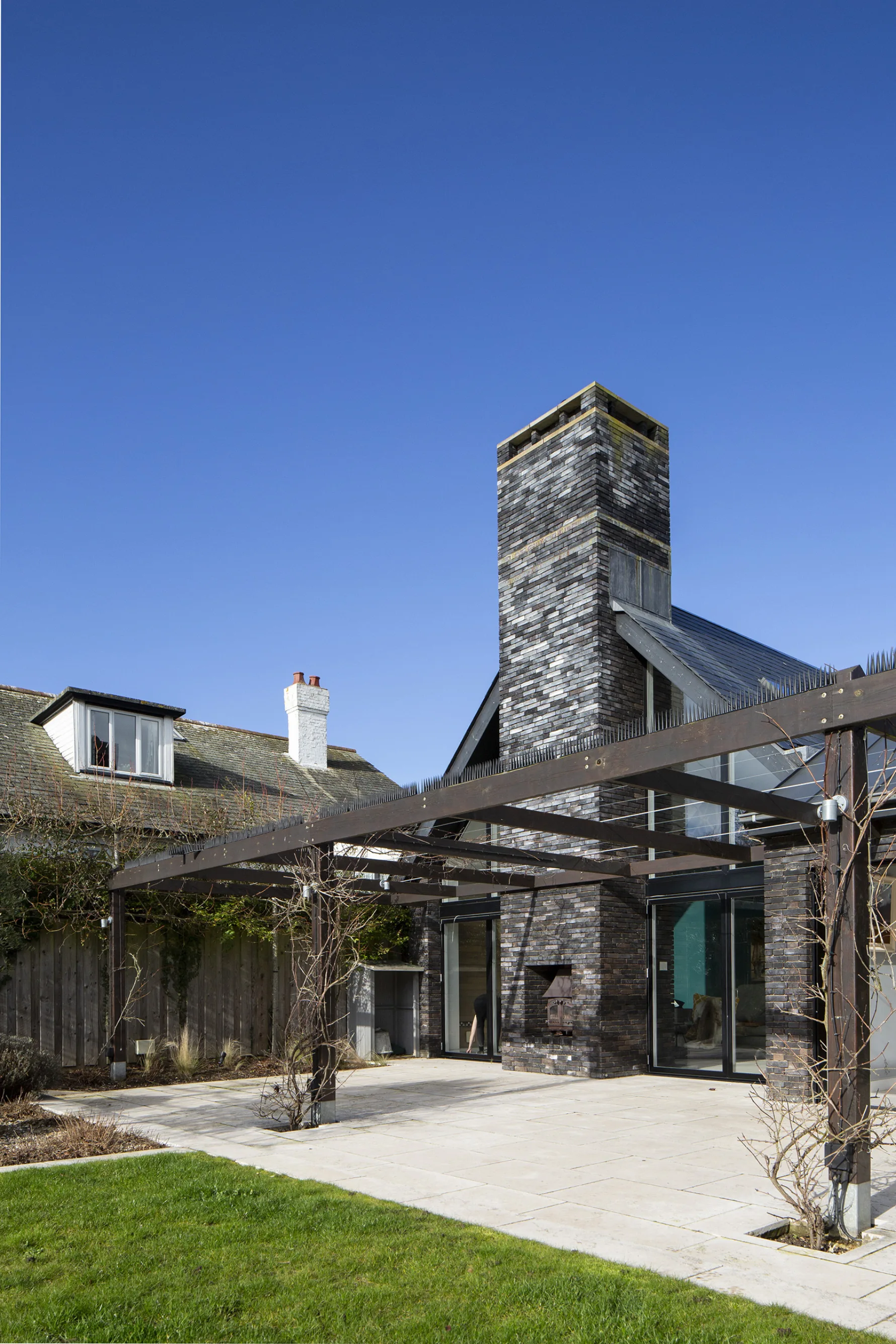 Contemporary rear extension with dark brick chimney and timber pergola structure in garden setting