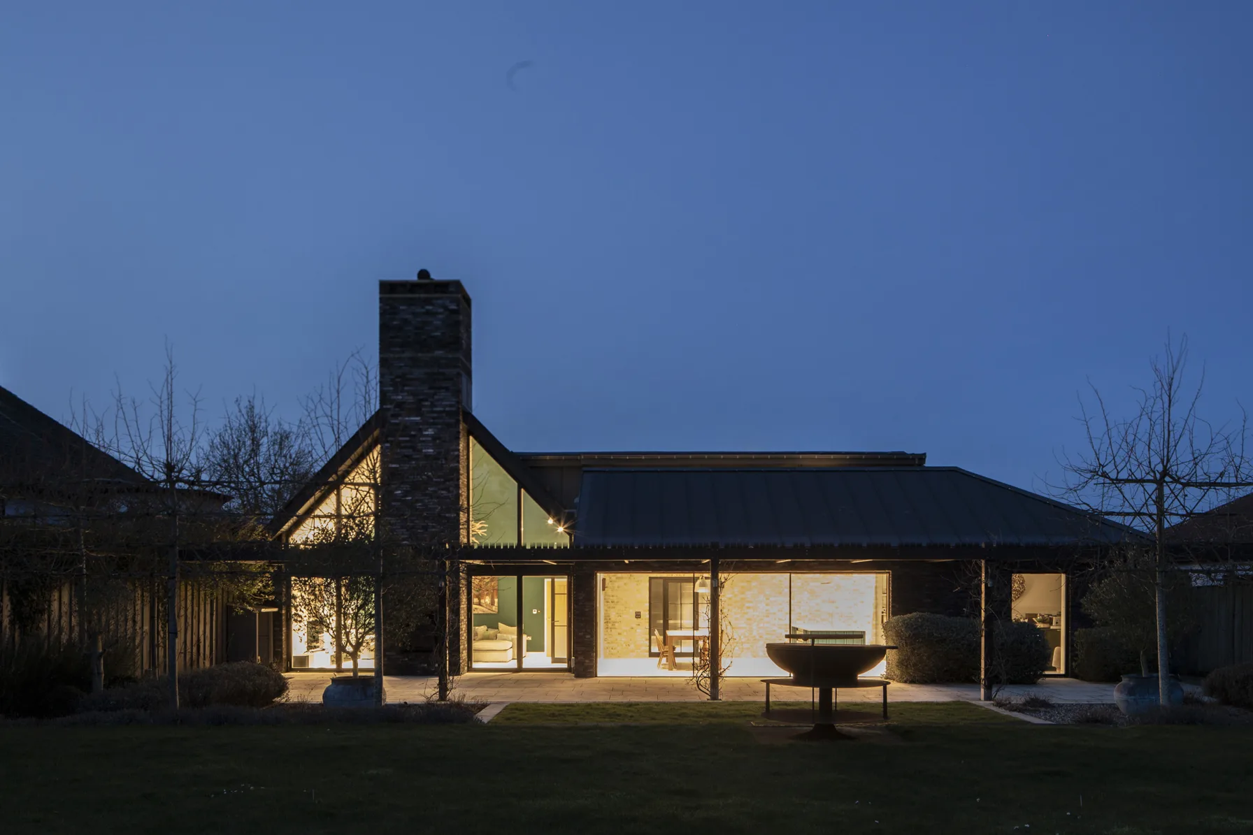 Rear elevation of contemporary house extension with large glazing and garden terrace illuminated at dusk in Old Hunstanton