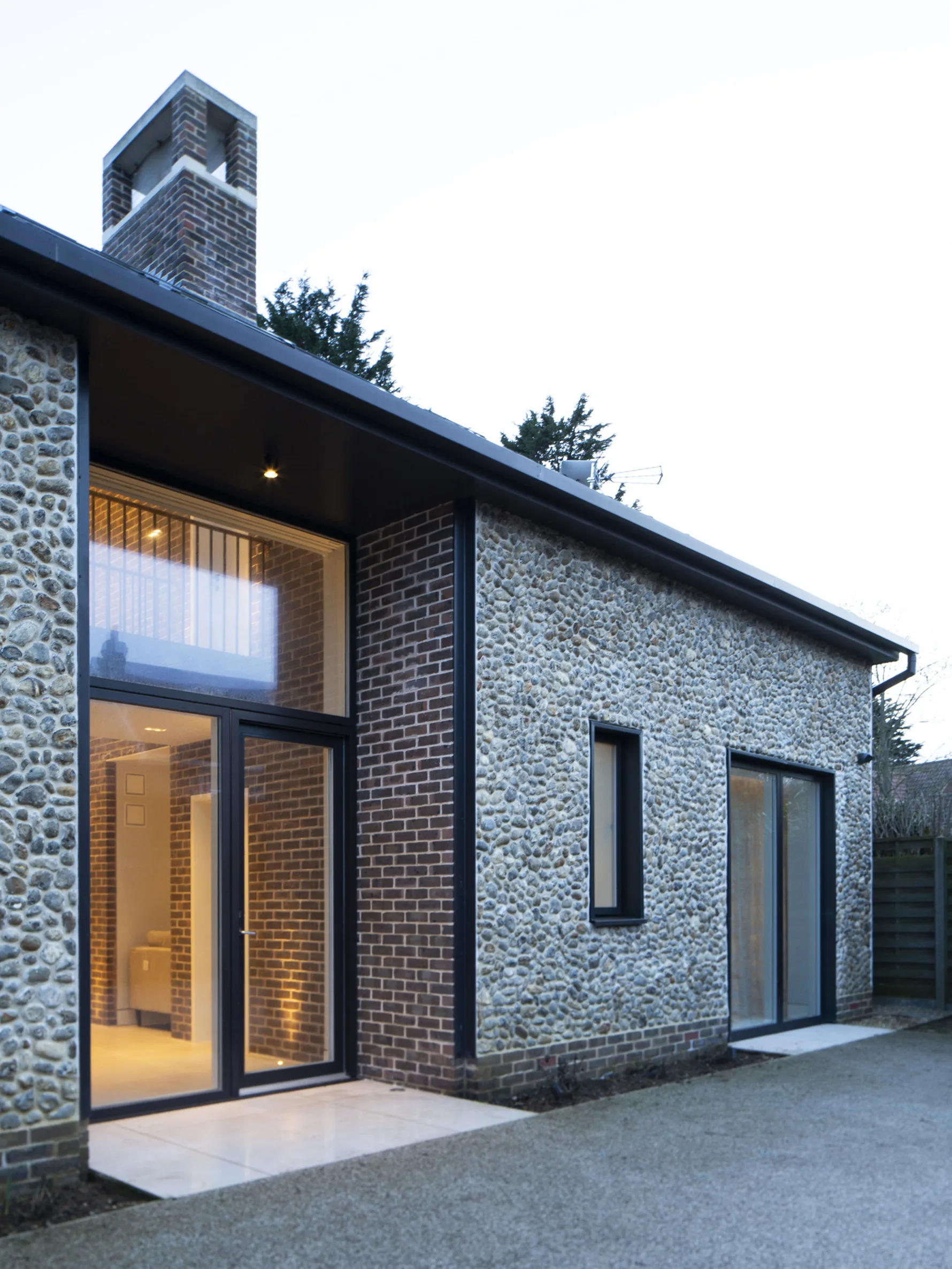 Contemporary house extension with flint and brick facade, large glazed doors and modern pitched roof