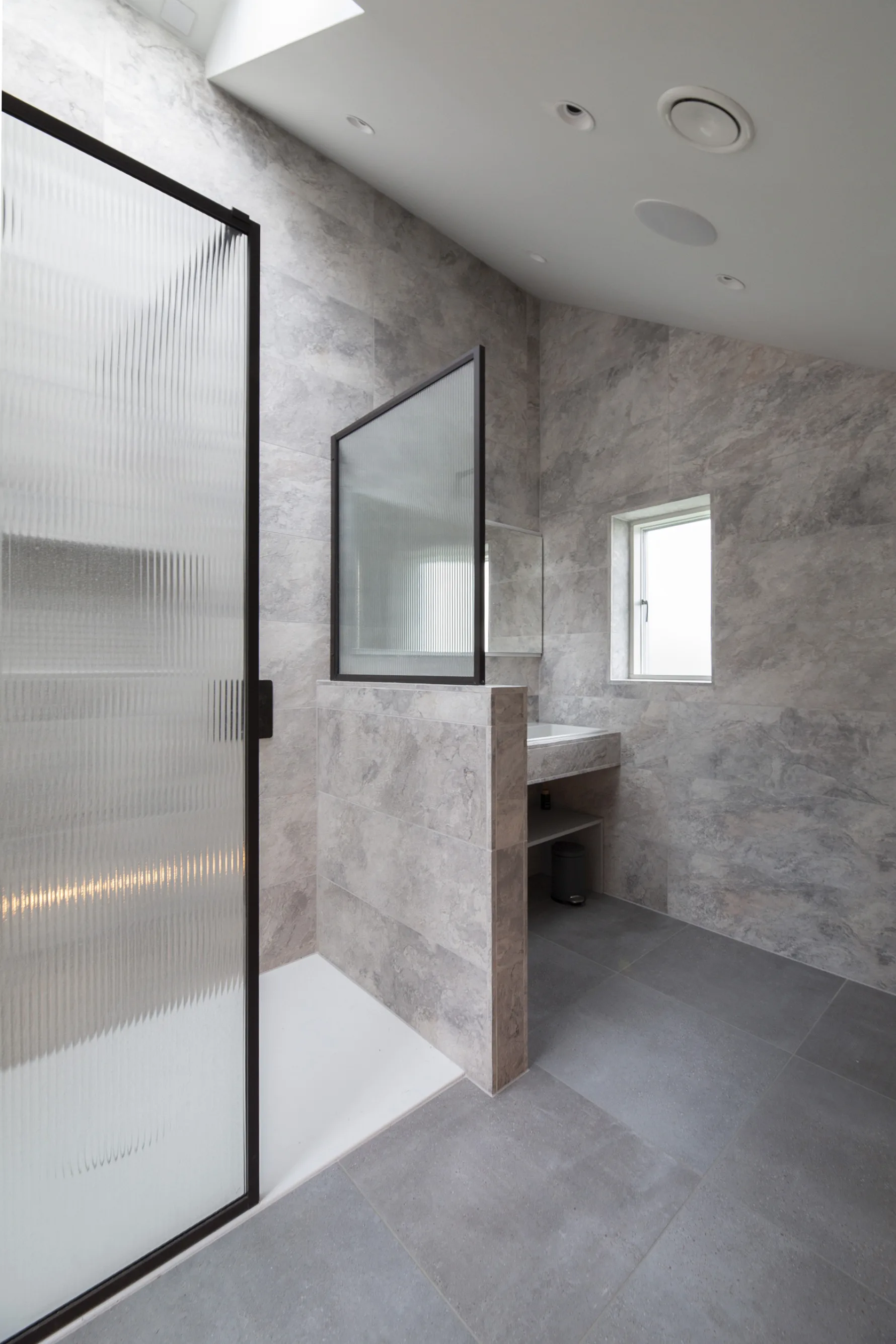 Contemporary ensuite bathroom in Old Hunstanton new build with stone tiles, walk-in shower and glazed screen