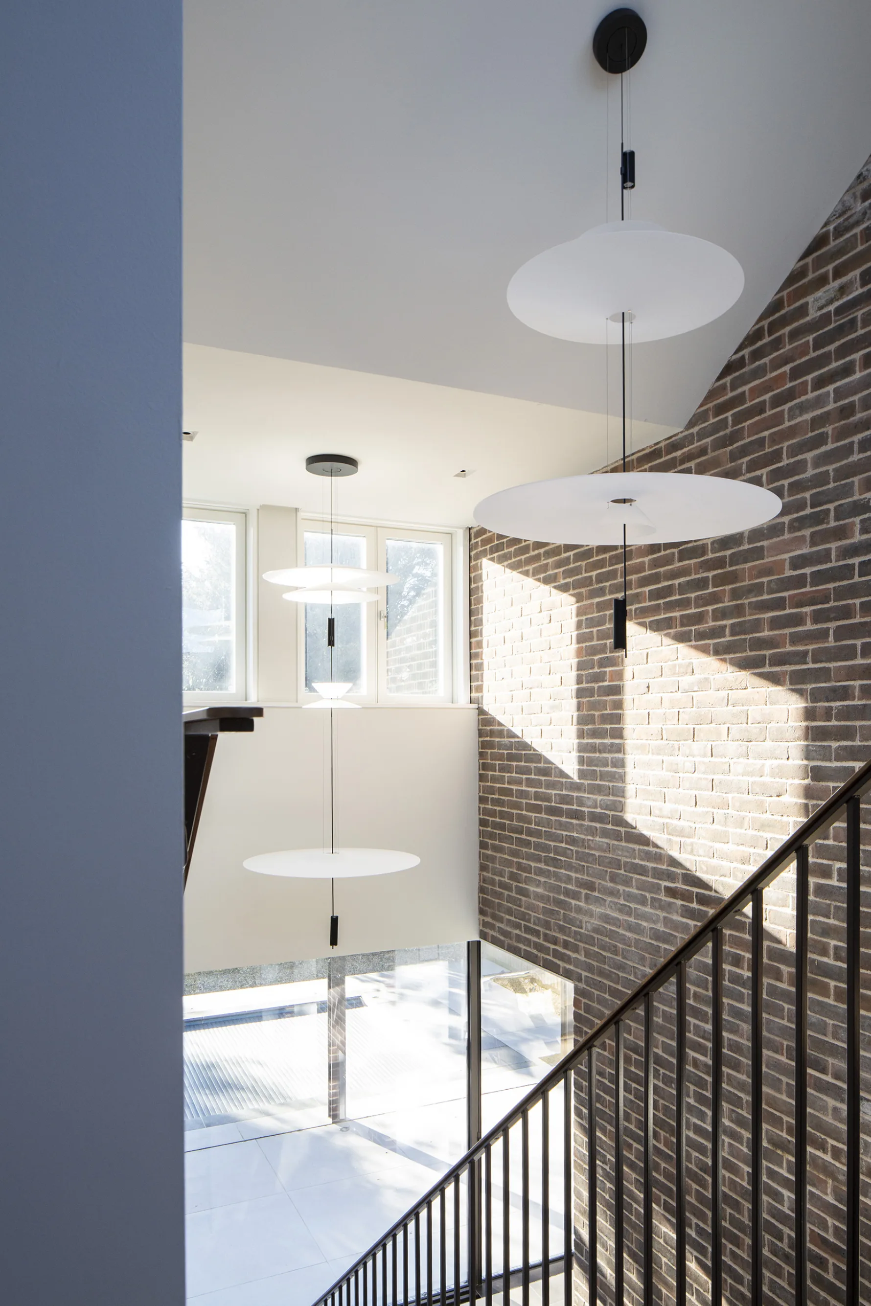 Double-height stairwell in Old Hunstanton new build with exposed brick wall, pendant lighting and large window