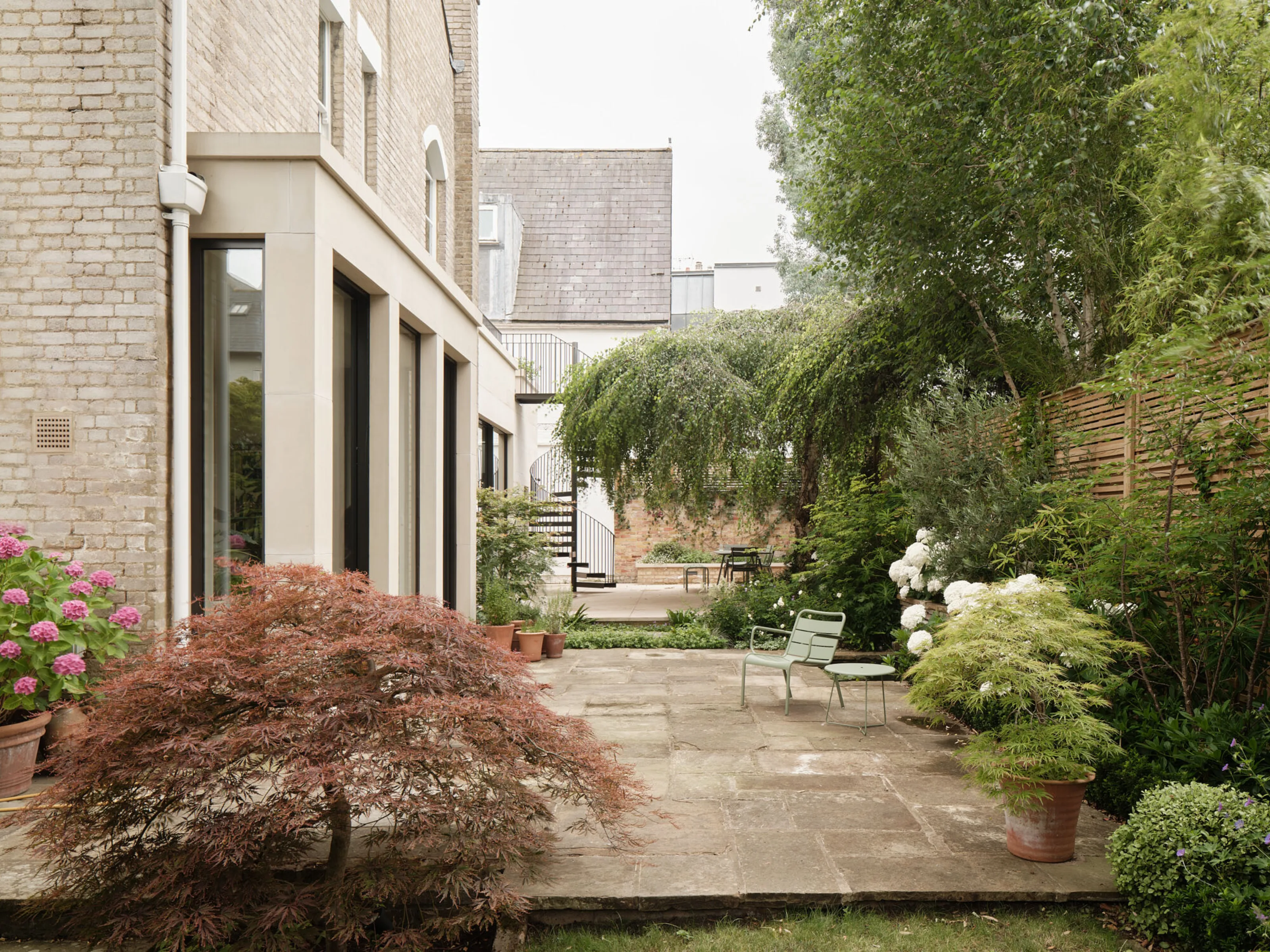 Landscaped rear garden with stone terrace, mature planting and views towards the contemporary extension of the Victorian house.