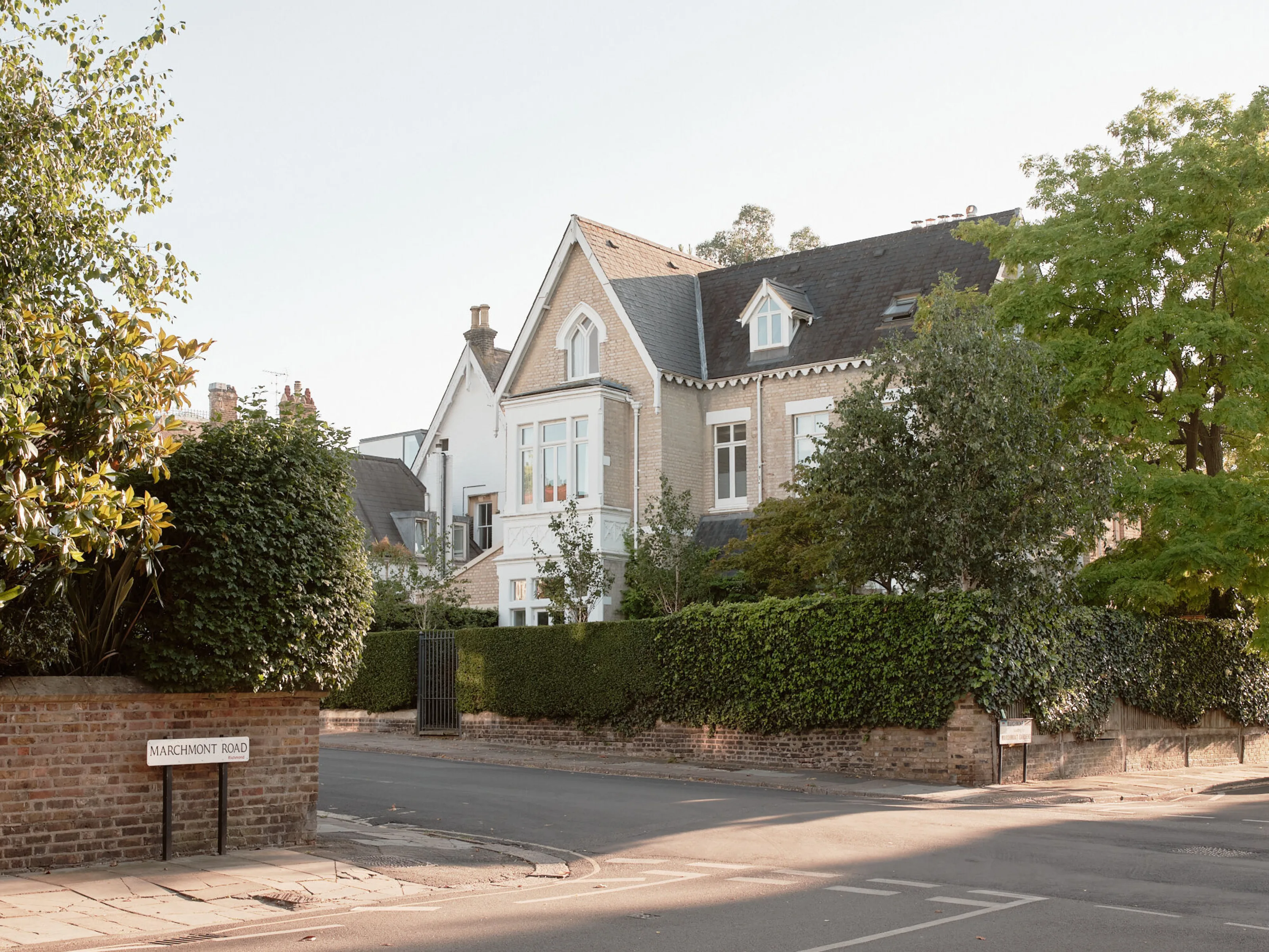 Street view of a restored Victorian house set behind hedges and mature trees on a residential corner site.