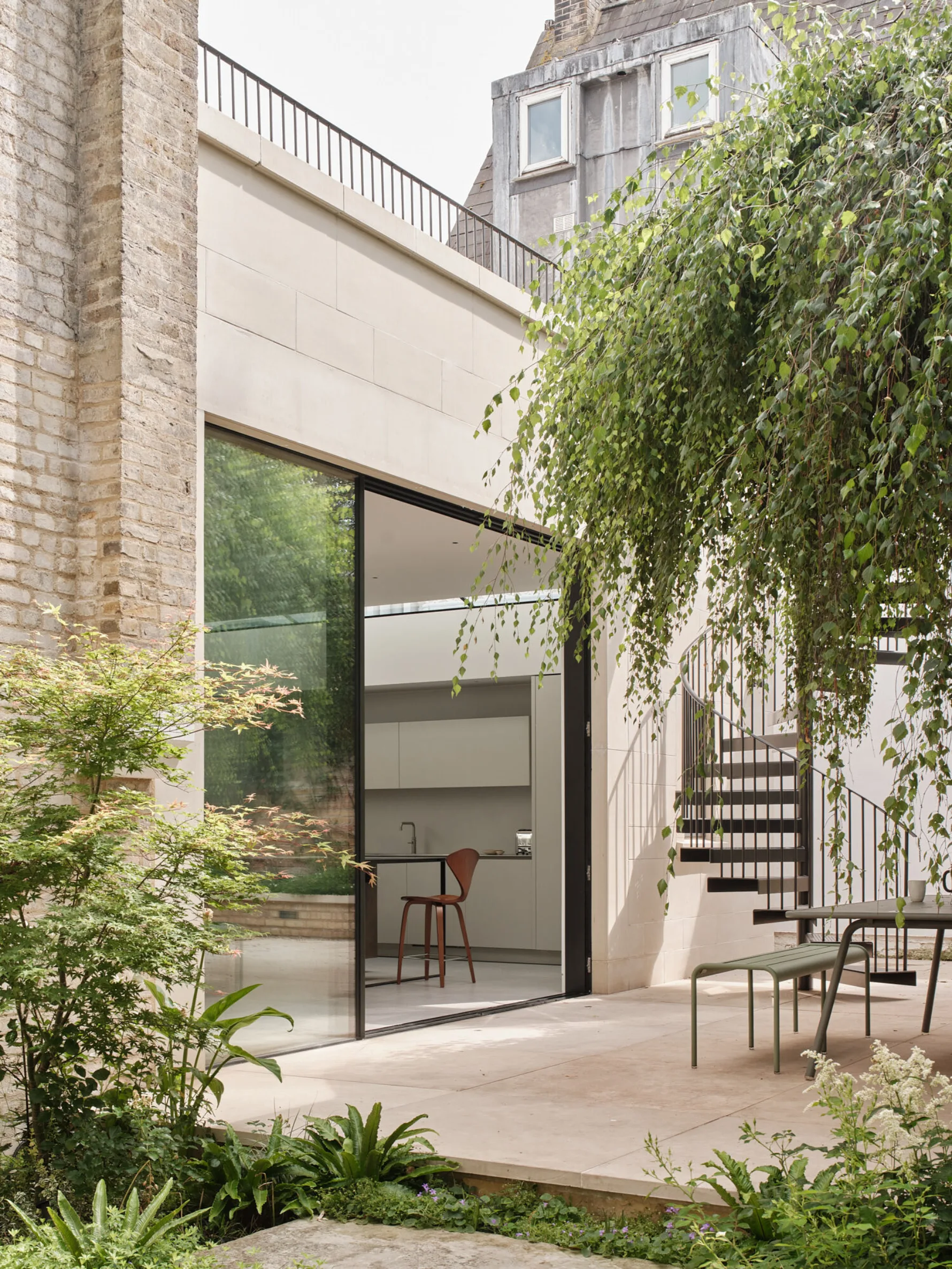 Courtyard garden with outdoor dining area beneath a mature weeping tree, framed by planting and the contemporary rear extension.