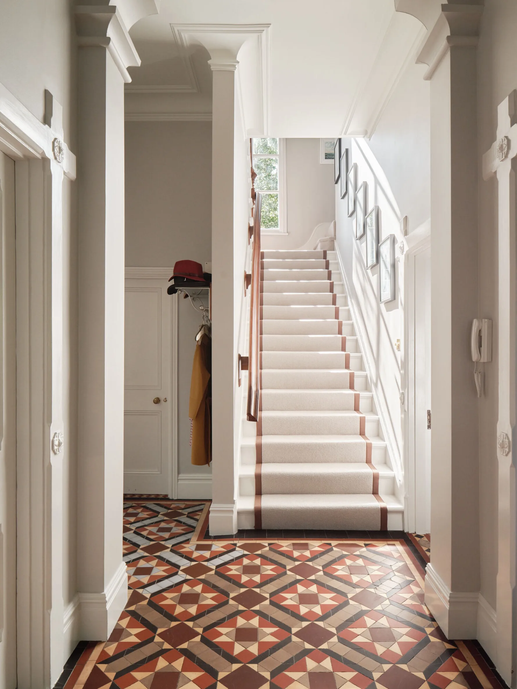 Entrance hall with original geometric tiled floor, decorative mouldings and staircase illuminated by natural light.