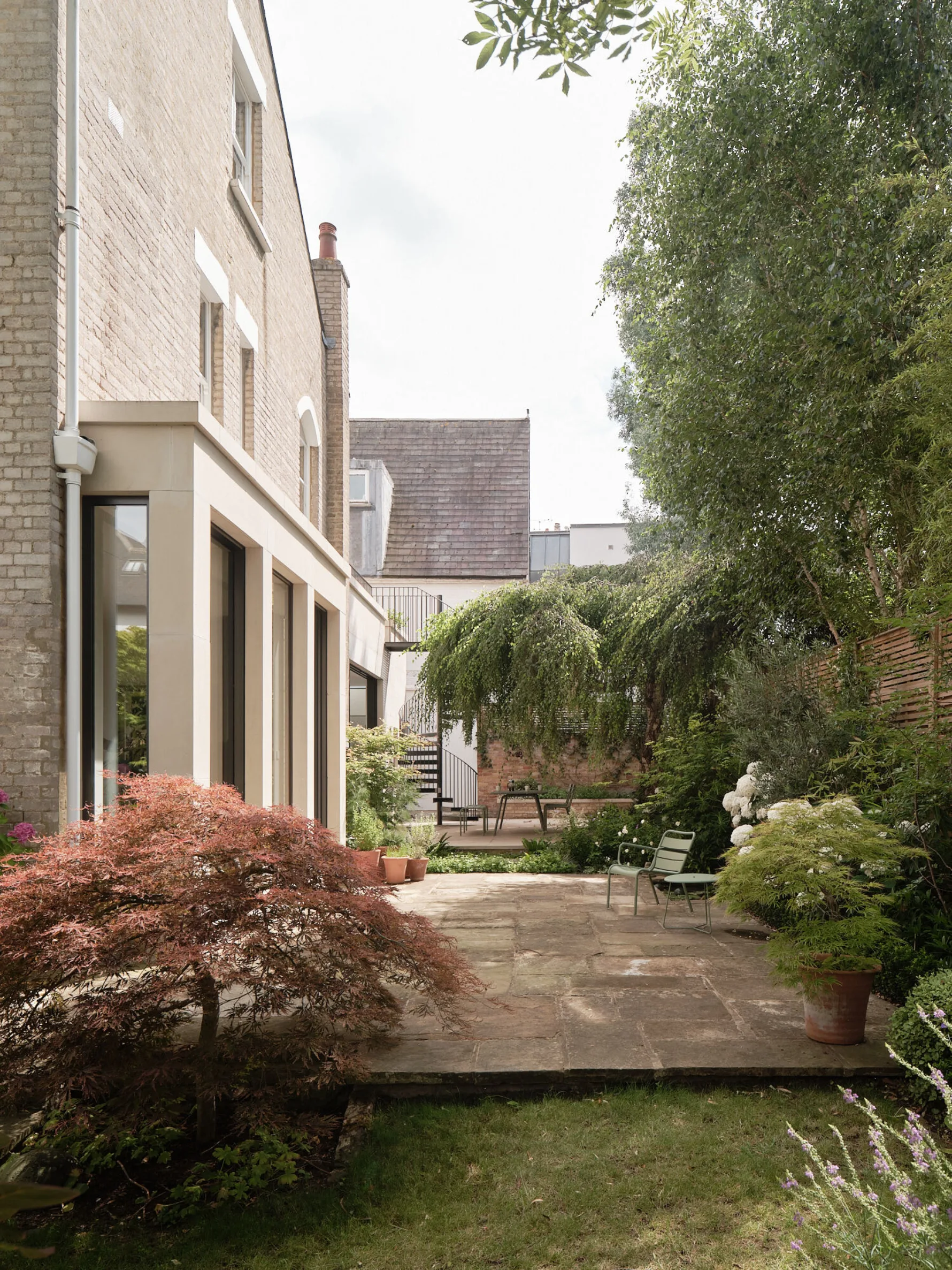 Courtyard garden with outdoor dining area beneath a mature weeping tree, framed by planting and the contemporary rear extension.