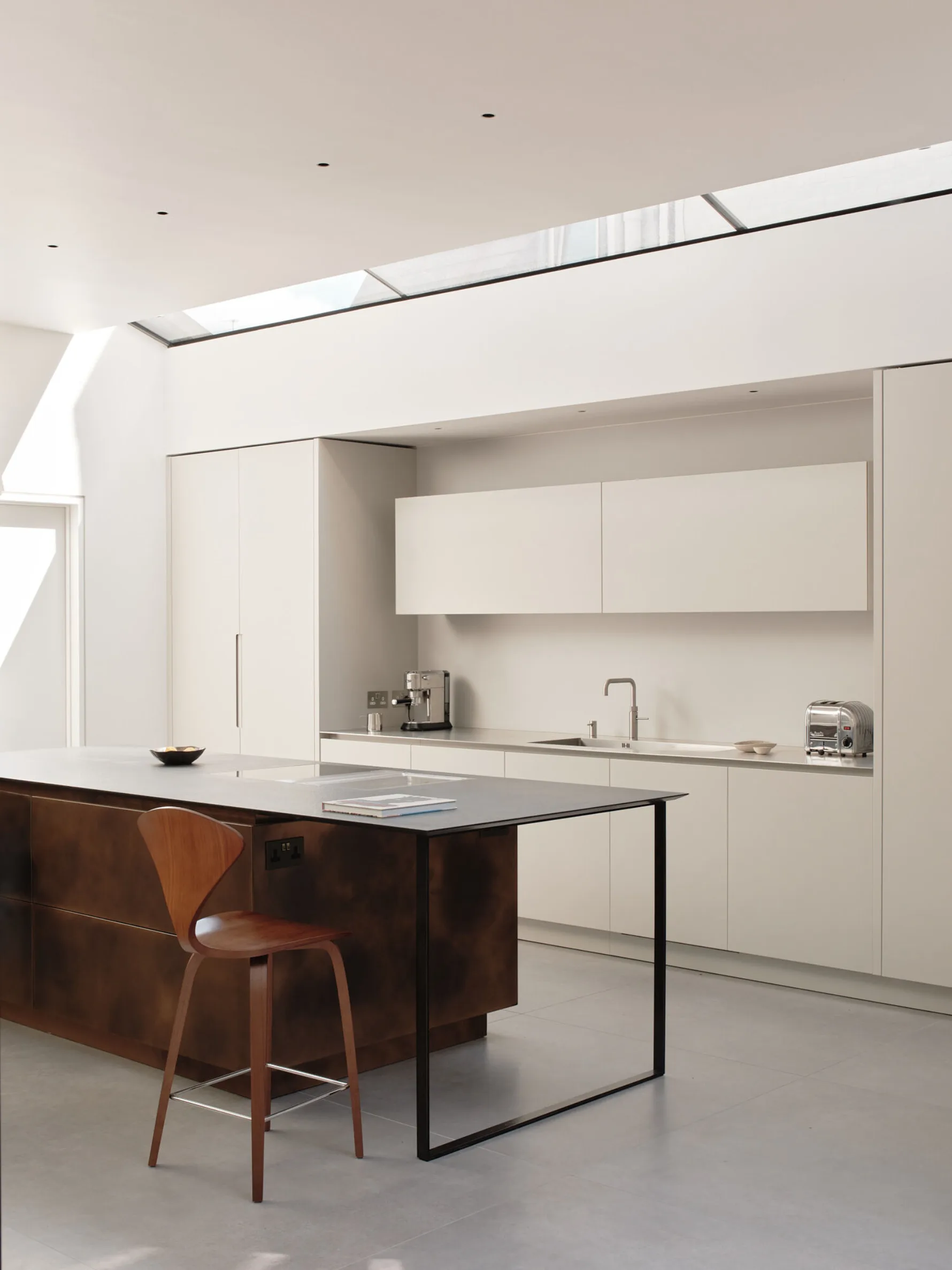 Contemporary kitchen with a dark metal-clad island, integrated breakfast bar, minimalist cabinetry and rooflights bringing daylight into the space.