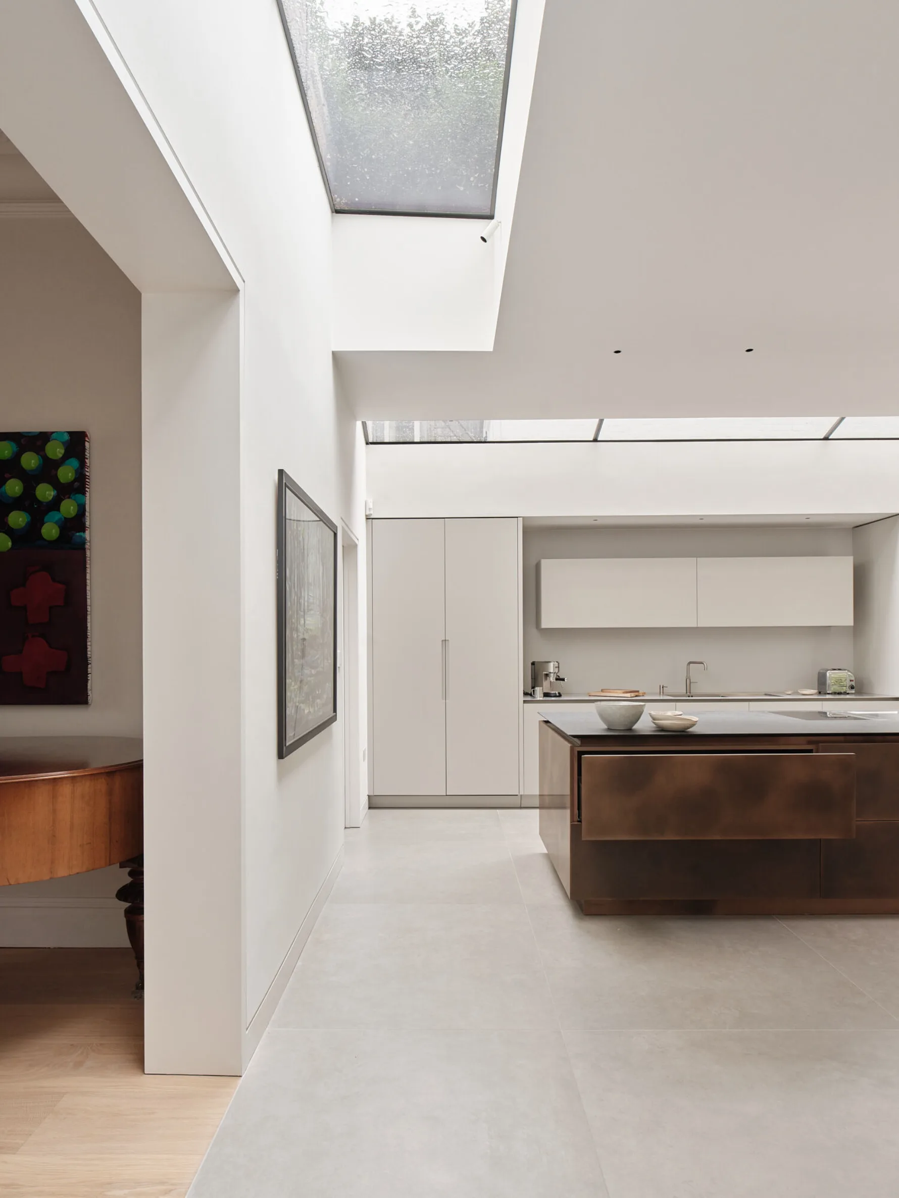 Minimalist kitchen illuminated by large rooflights, featuring a dark metal island and concealed cabinetry within the contemporary extension.