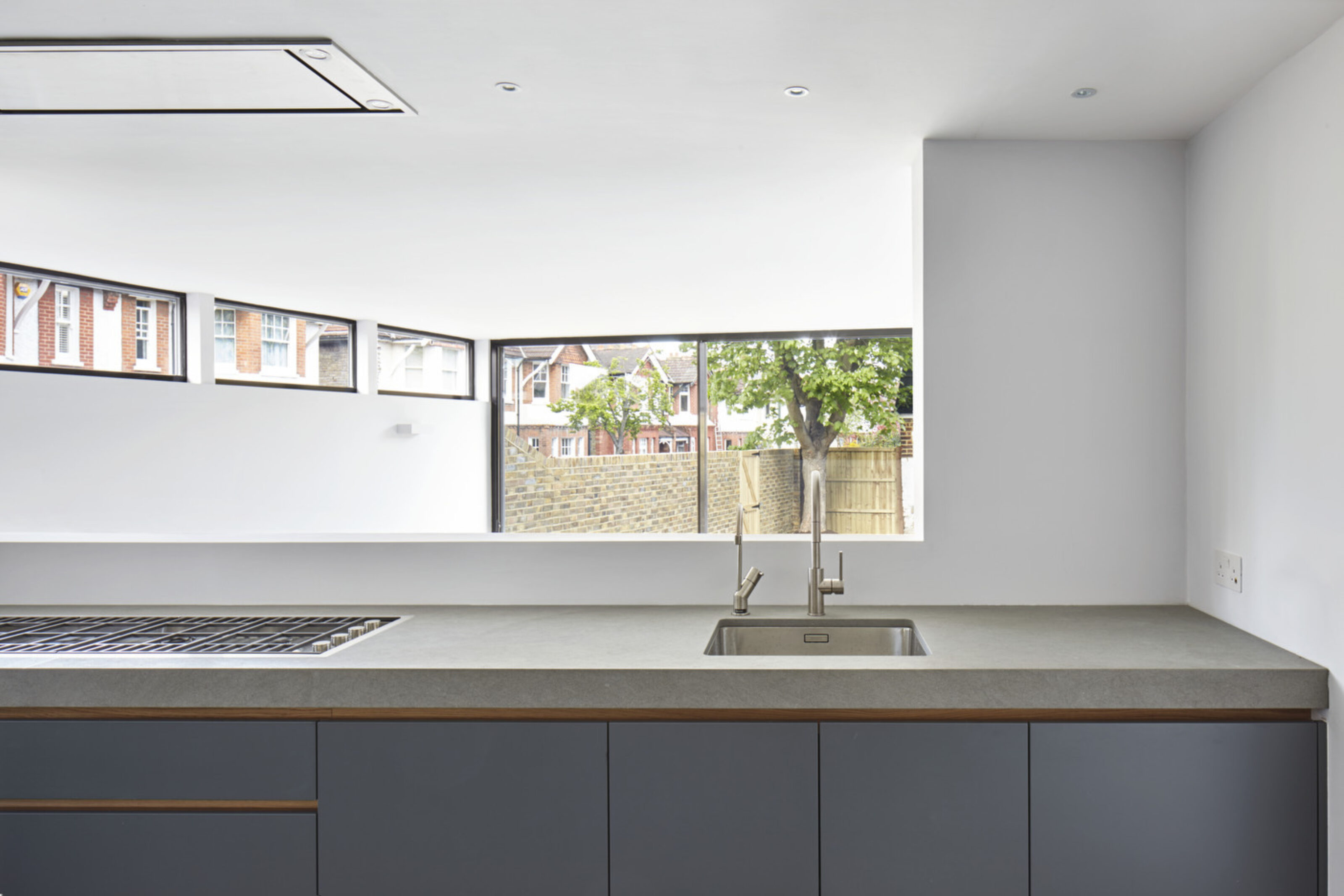 Contemporary kitchen extension at Twickenham House with bespoke cabinetry, concrete worktops and large garden-facing windows.