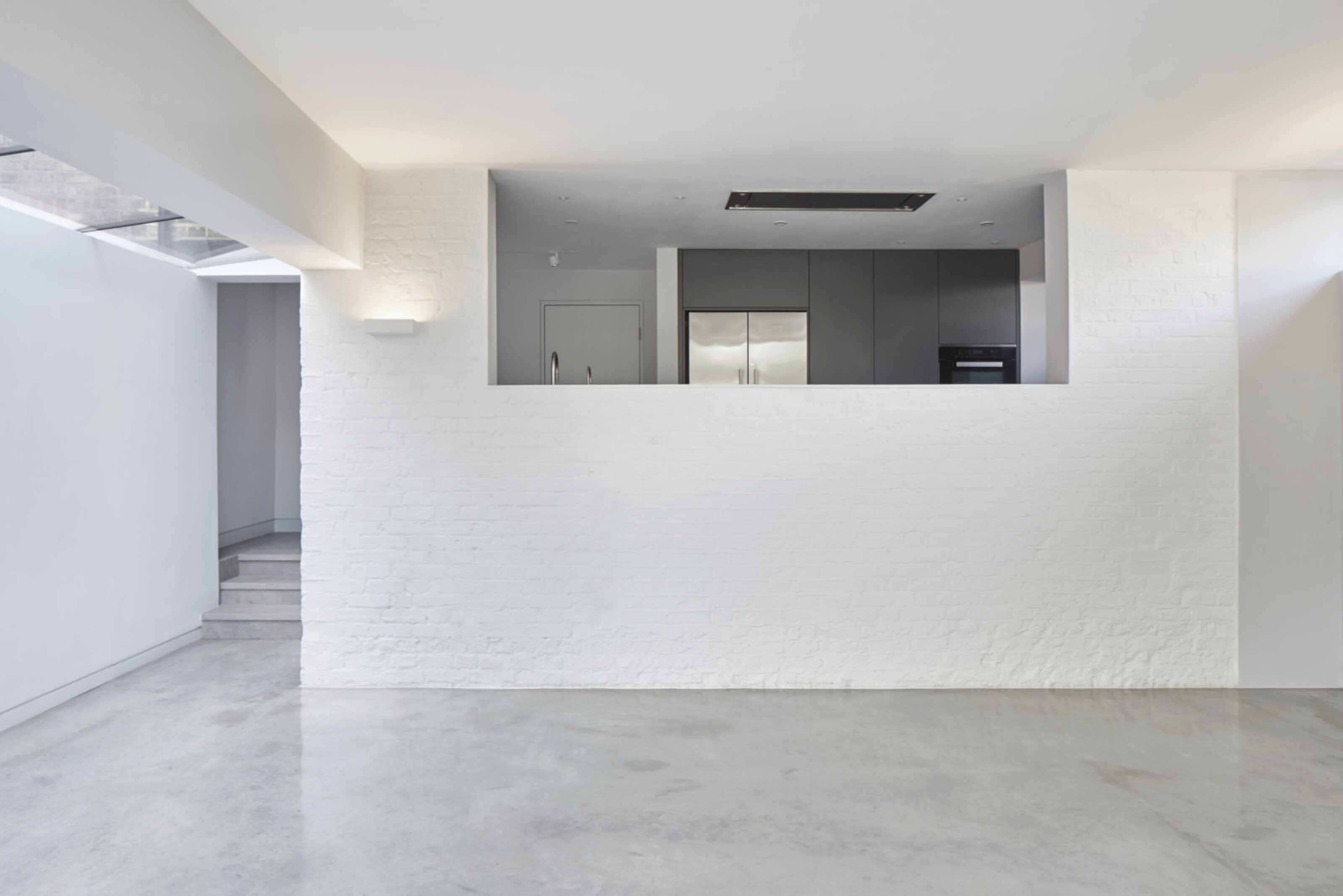 Open-plan kitchen and living area at Twickenham House featuring exposed brickwork, polished concrete flooring and bespoke cabinetry.