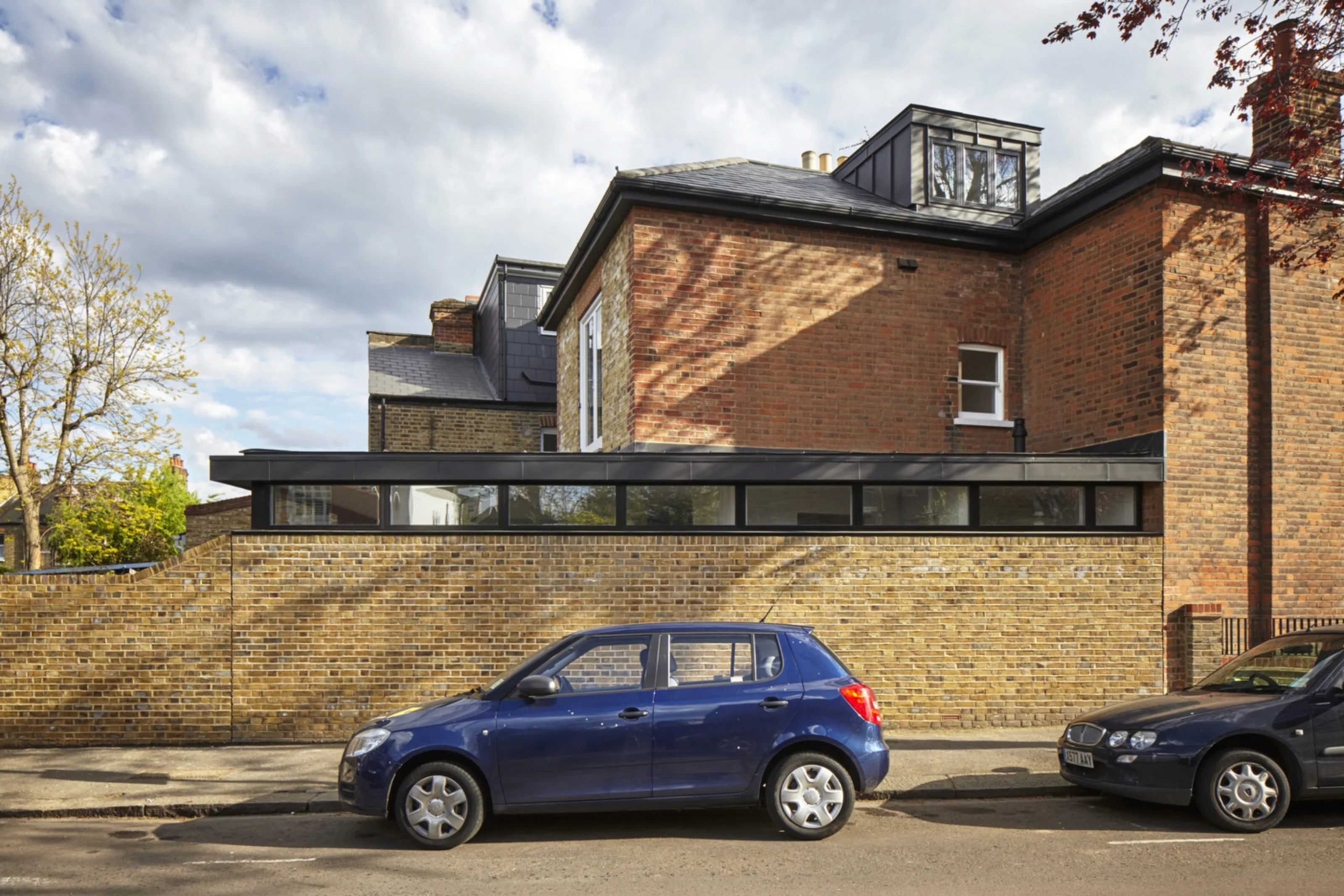 Rear elevation of Twickenham House showing a contemporary single-storey extension with clerestory glazing and brick boundary walls.