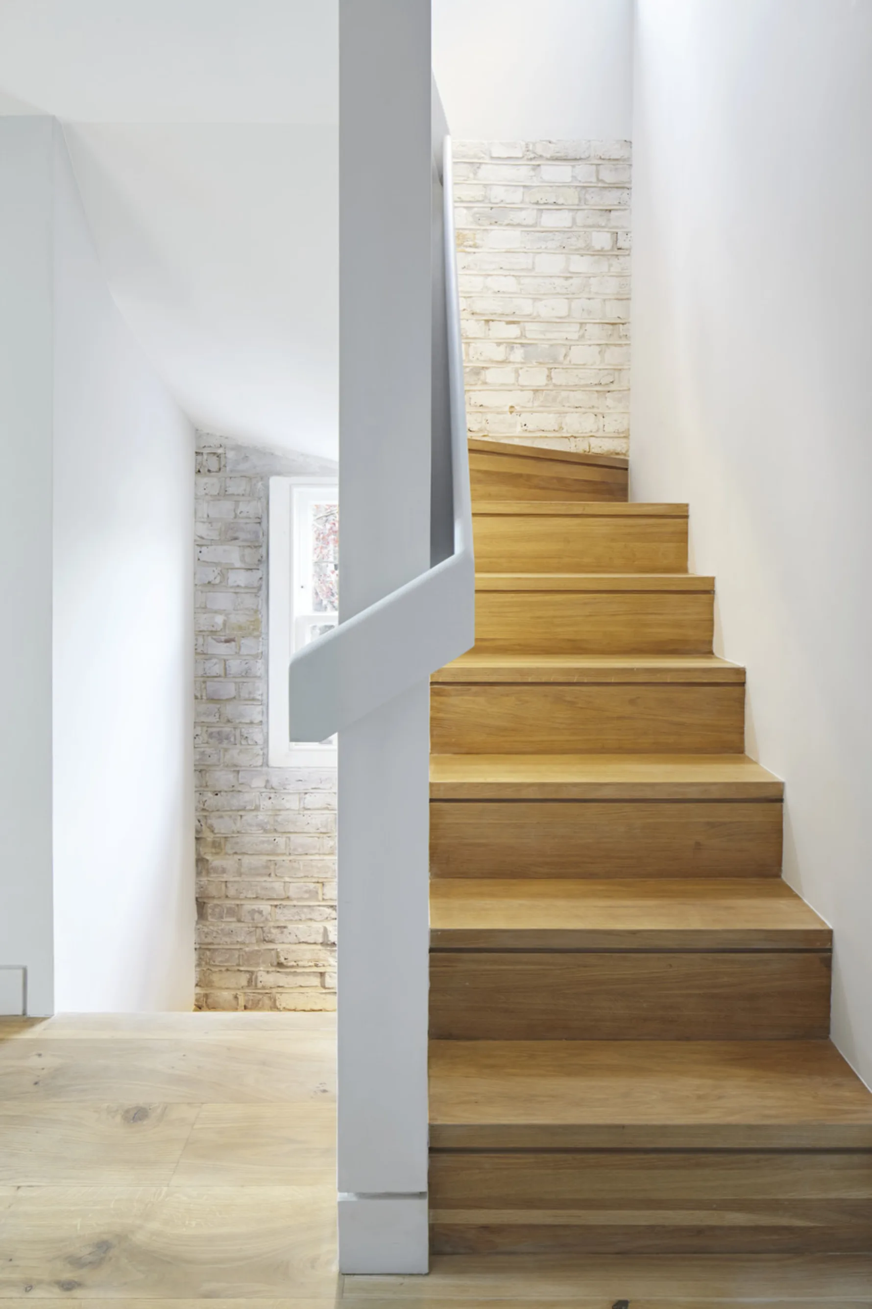 Bespoke oak staircase at Twickenham House featuring exposed painted brickwork and contemporary architectural detailing.