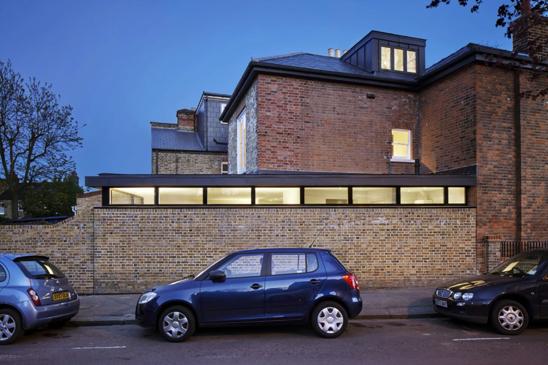 Twickenham House at twilight featuring a contemporary rear extension with horizontal glazing, zinc cladding and restored Victorian brickwork.